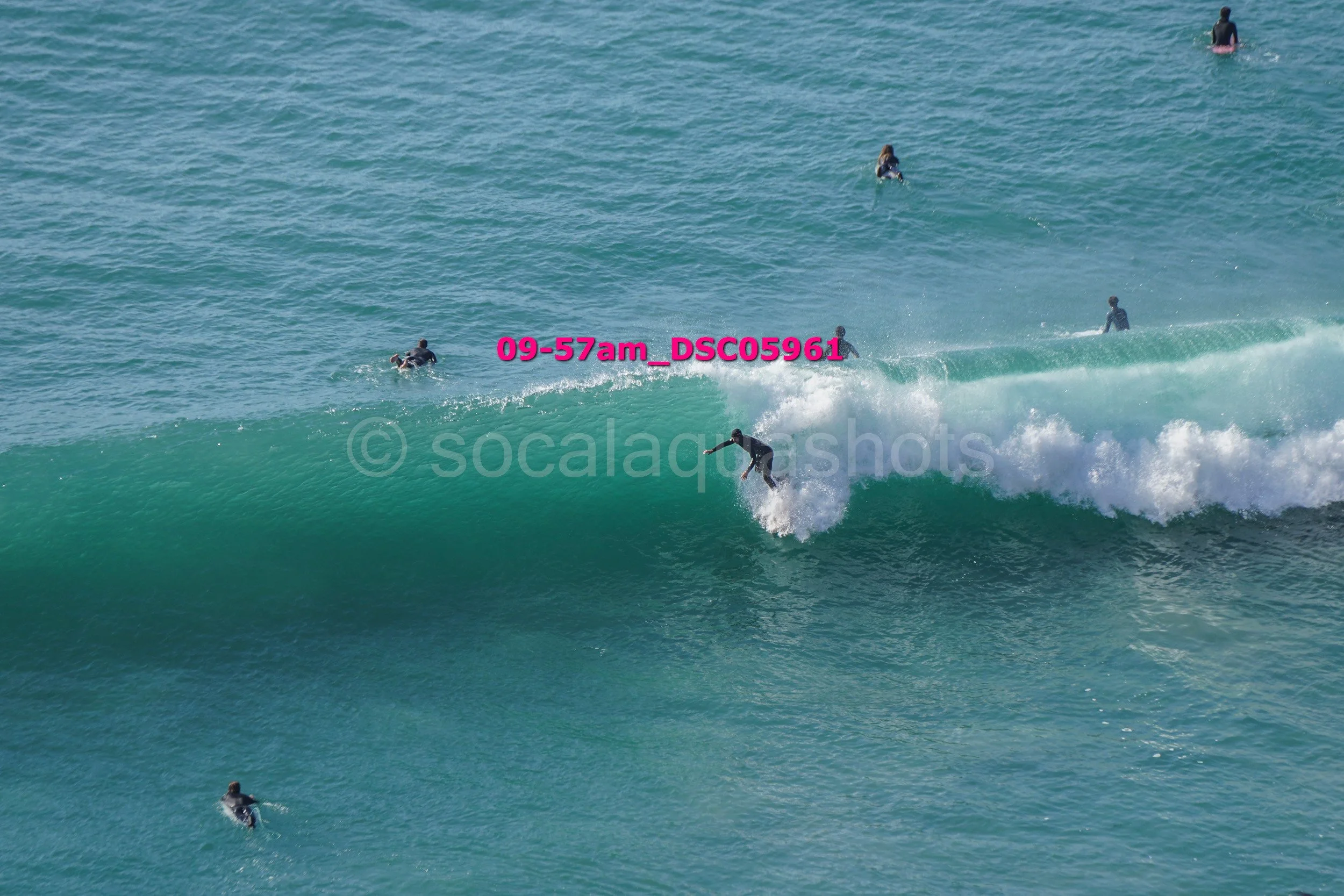 Surfer riding a wave with several other surfers in the water around him.