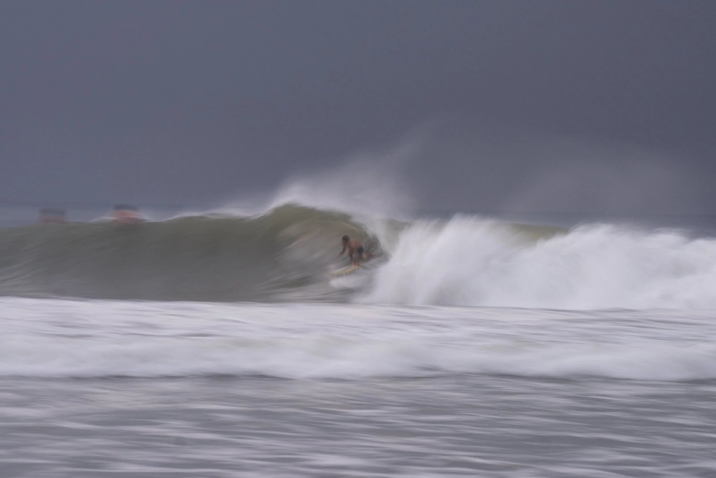A surfer riding a wave in stormy weather with dark clouds in the sky.