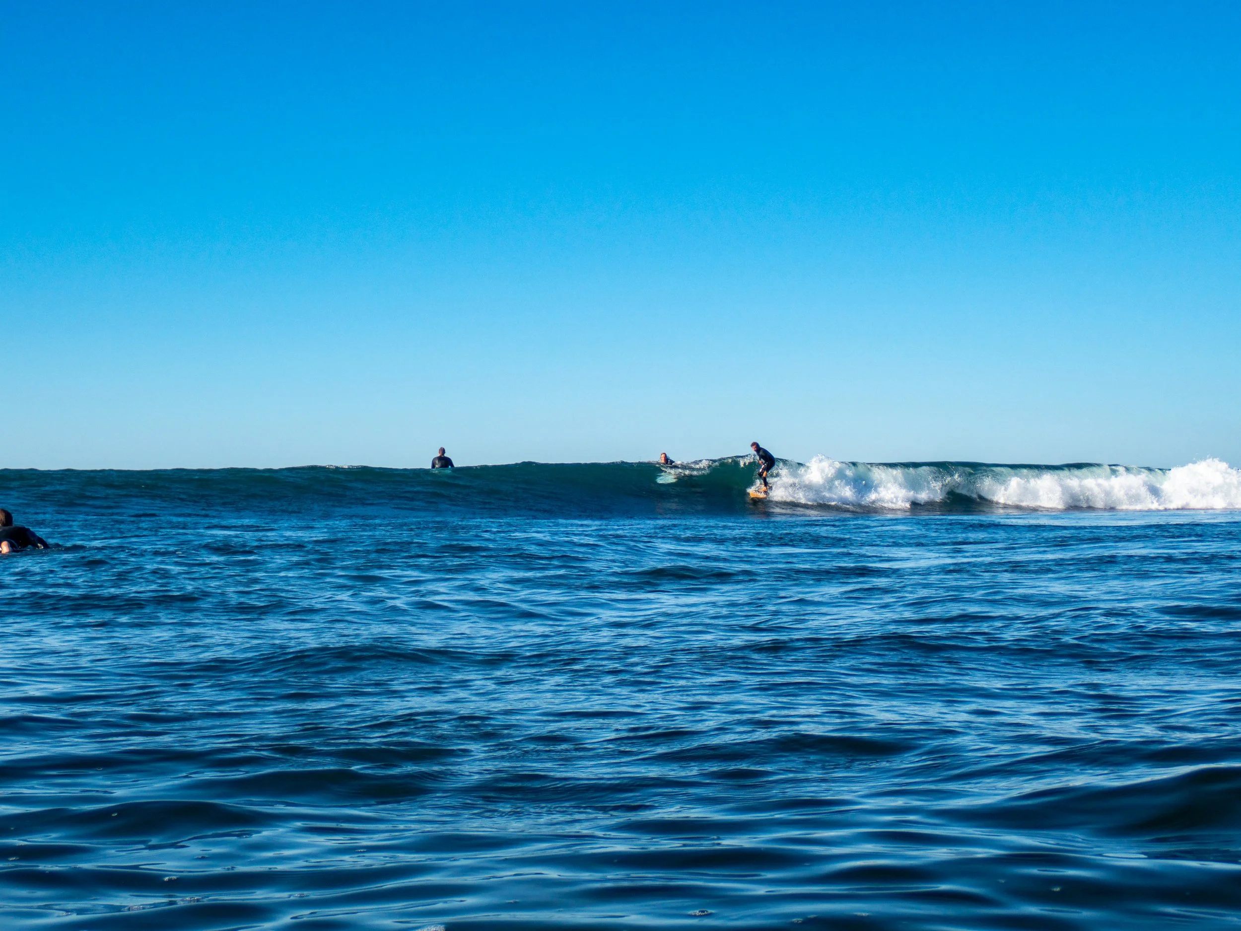 People surfing on the ocean waves under a clear blue sky.