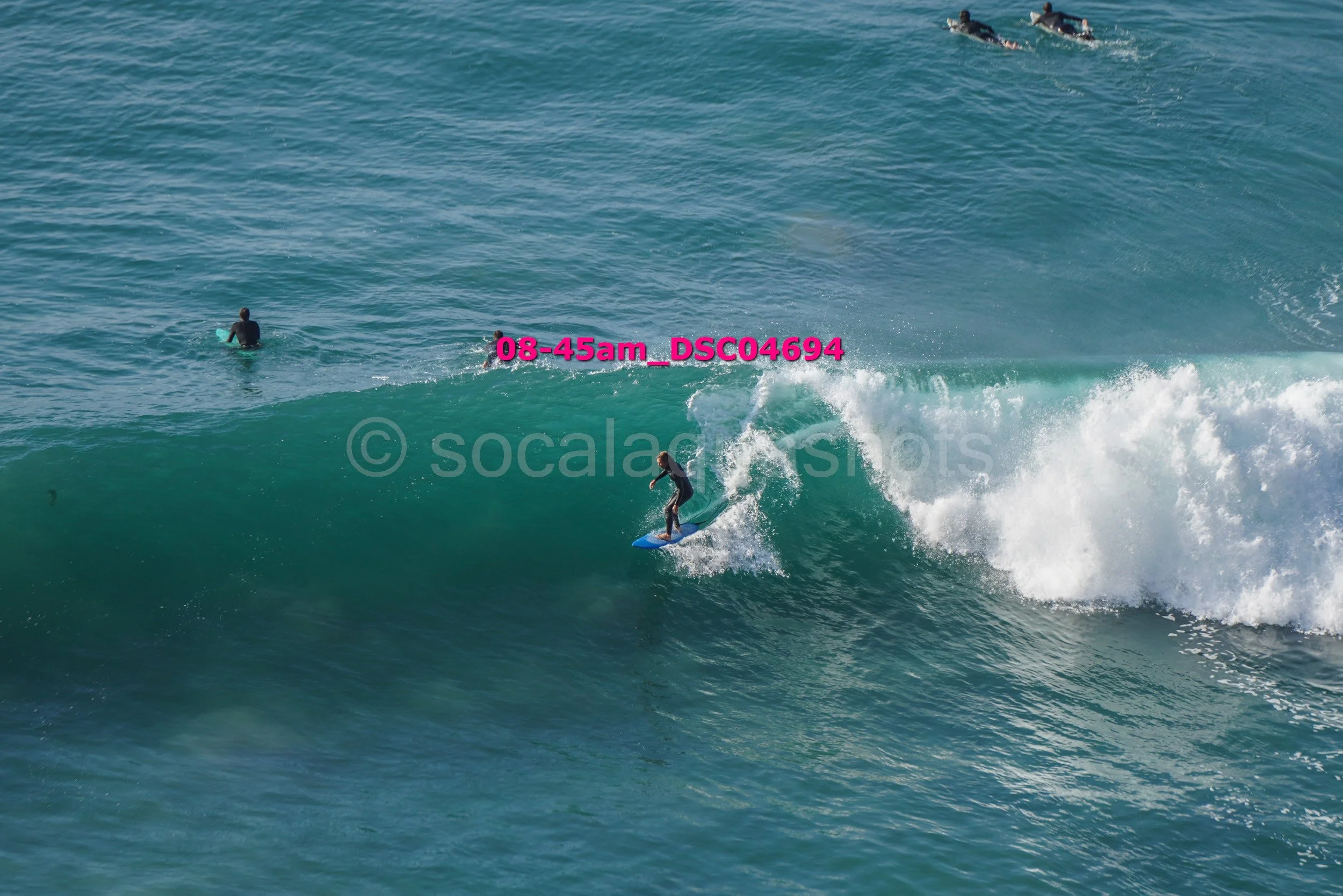Surfer riding a wave in the ocean with other surfers in the distance.