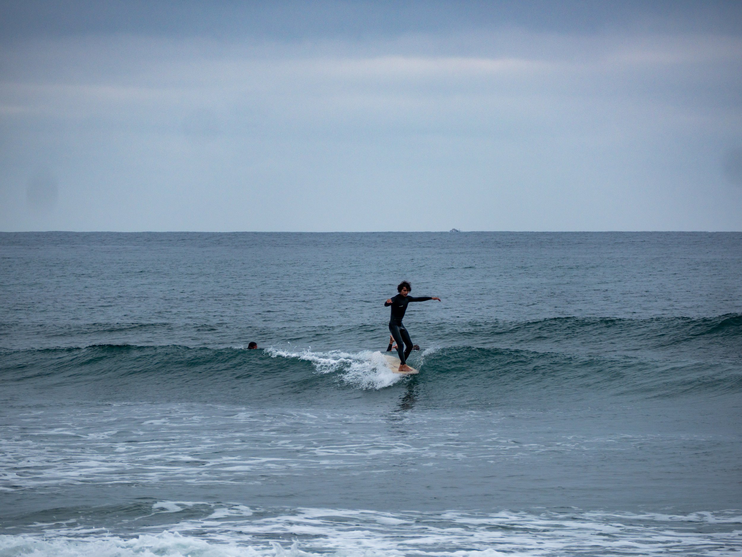 Person surfing on a small wave in the ocean under a cloudy sky.