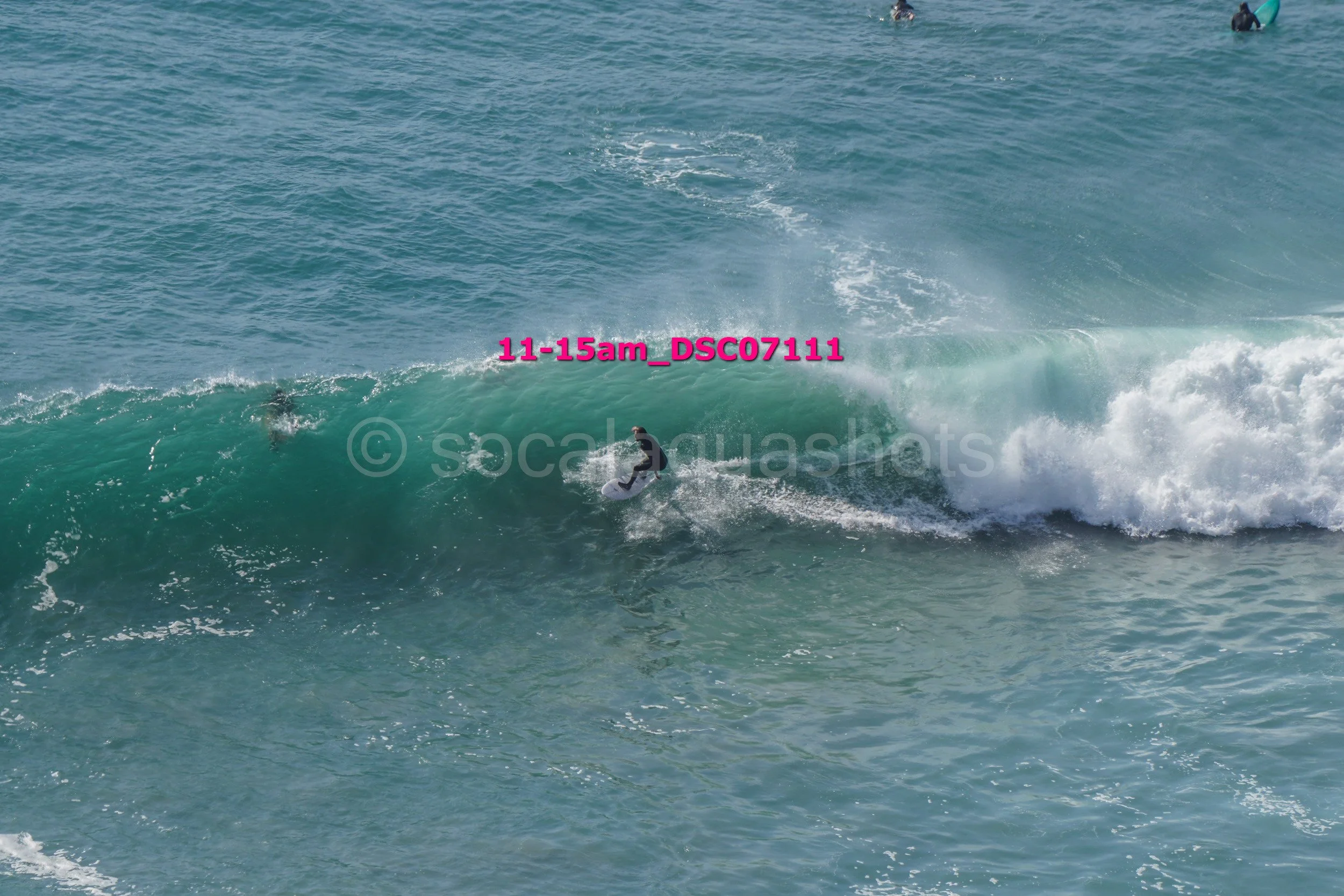 A person surfing on a large wave in the ocean with others in the water in the background.