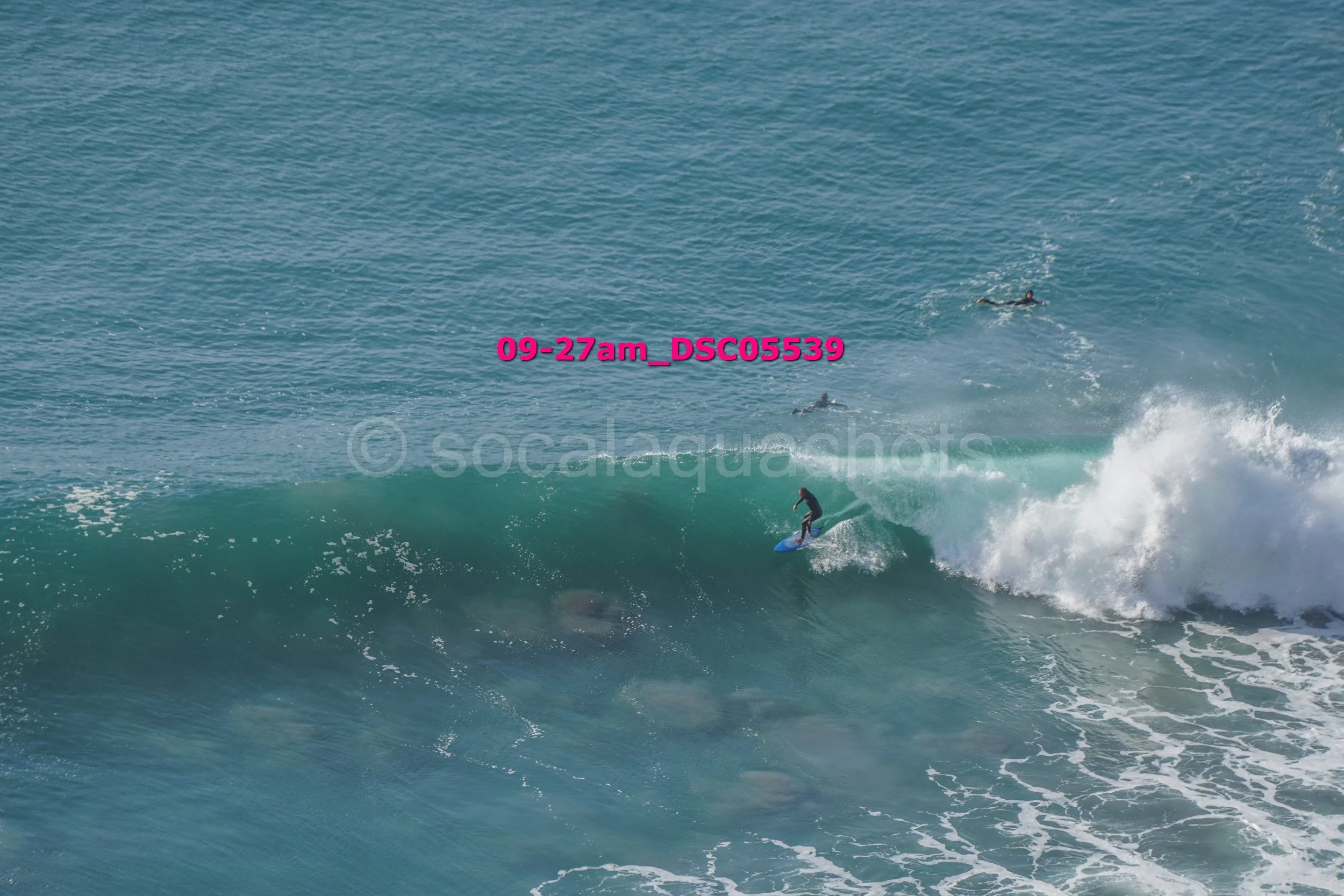 Person surfing on a large wave in the ocean with two other surfers in the distance.