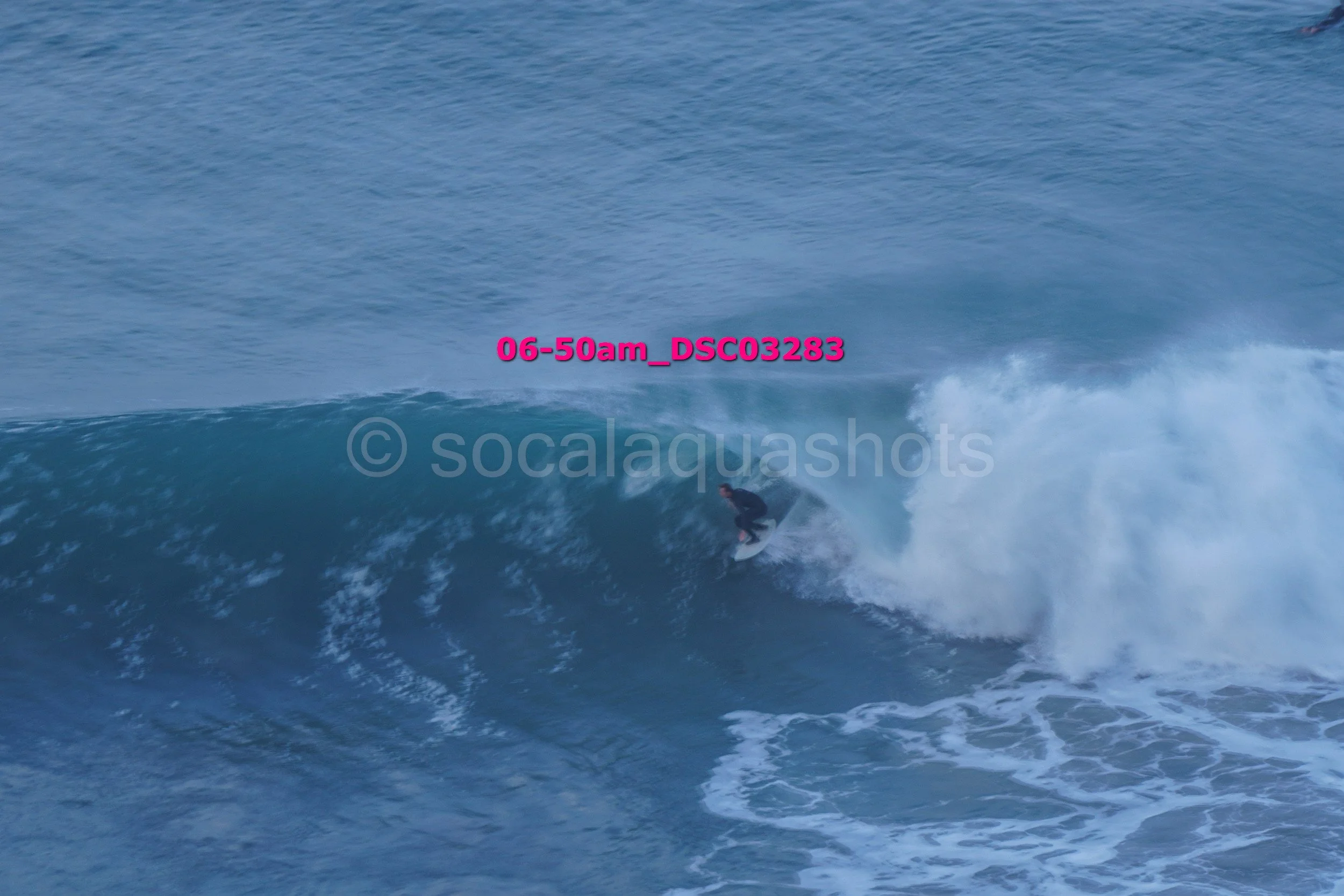 A person surfing on a large ocean wave in the early morning.