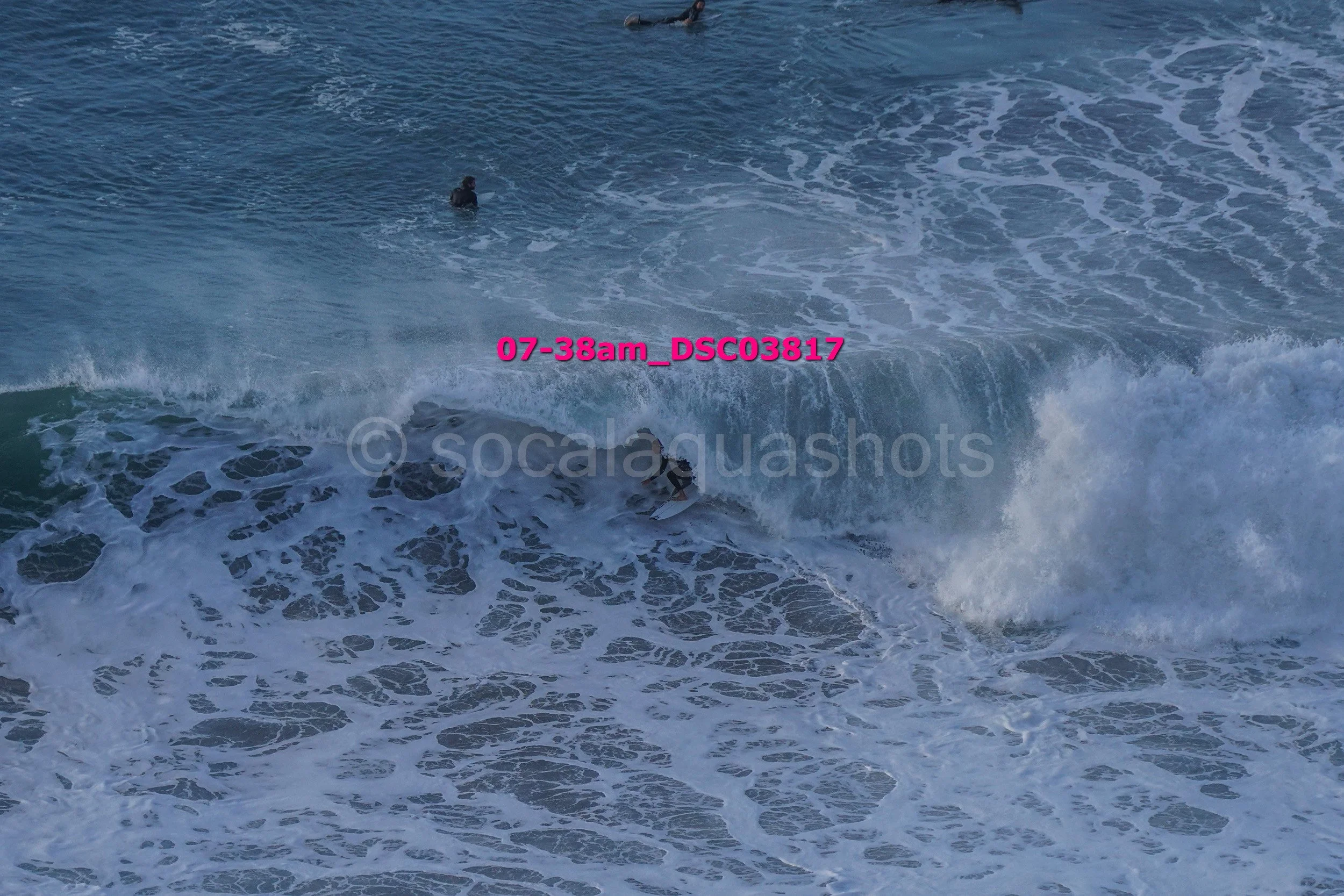 A person surfing on a wave in the ocean with a few other people swimming nearby.