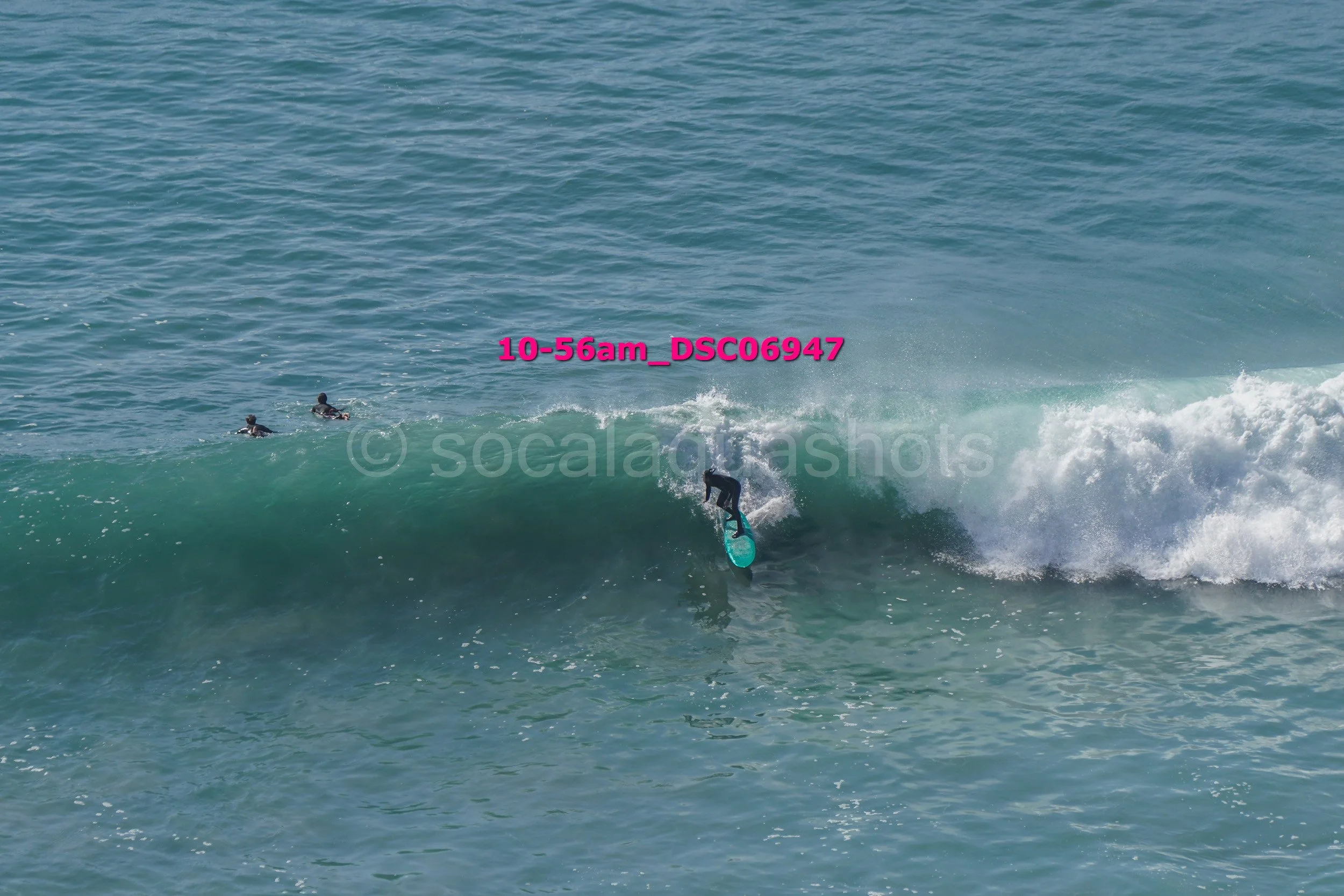 A person surfing on a wave with two other surfers in the distance in the ocean.