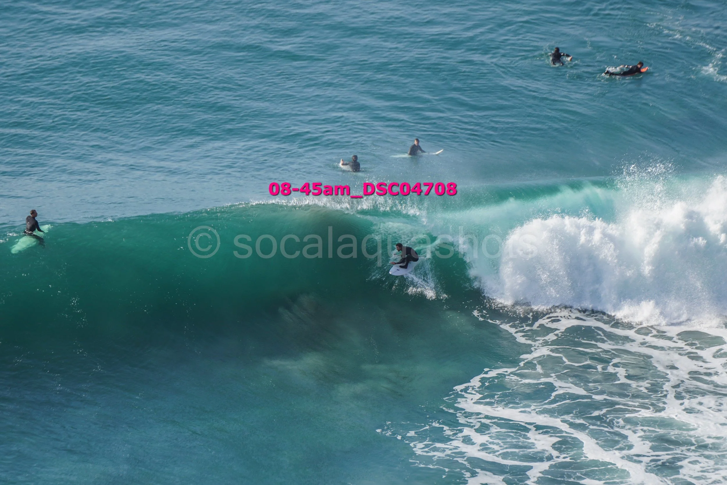 Surfer riding a large wave with several surfers in the background in the ocean.