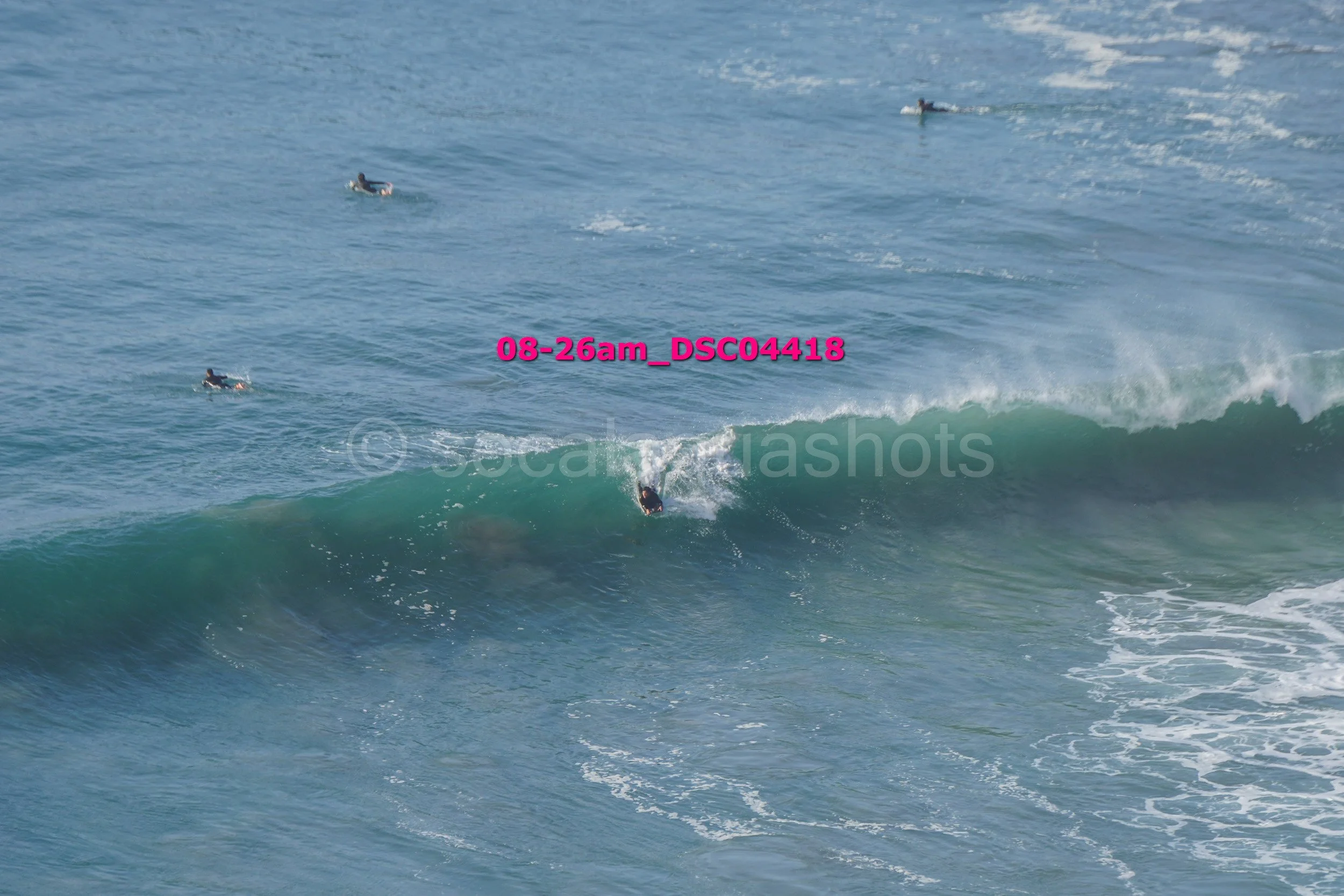 A surfer riding a wave in the ocean with three other surfers in the water nearby.