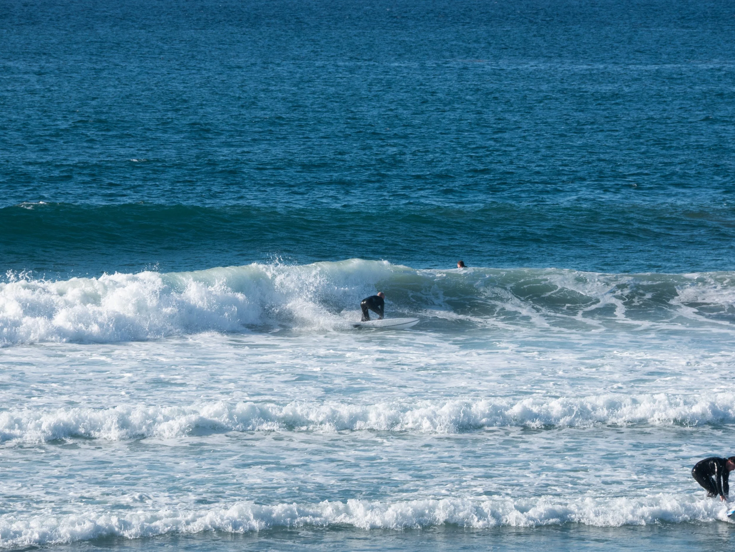 People surfing on the ocean waves, with one person riding a wave on a surfboard and another person in the water nearby.