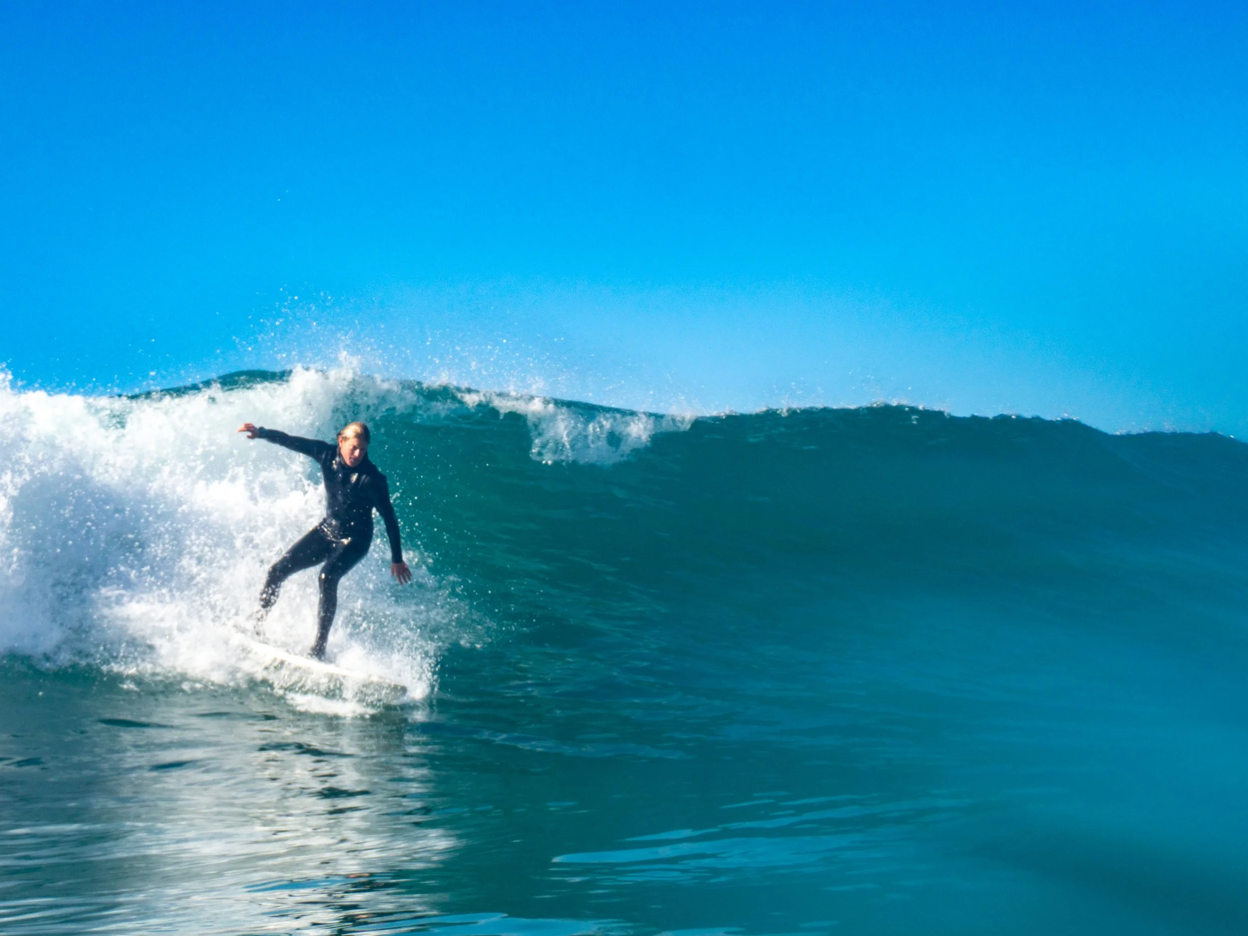 A person surfing on a wave in the ocean on a clear day.