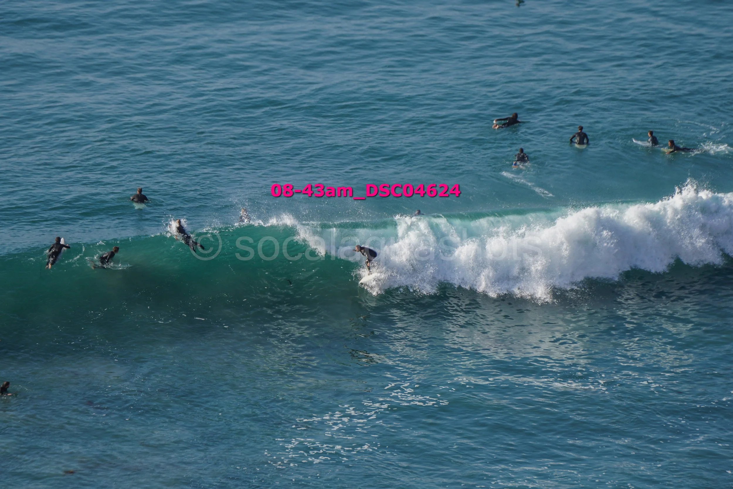 Surfers riding a wave in the ocean, with several people in the water waiting for waves.