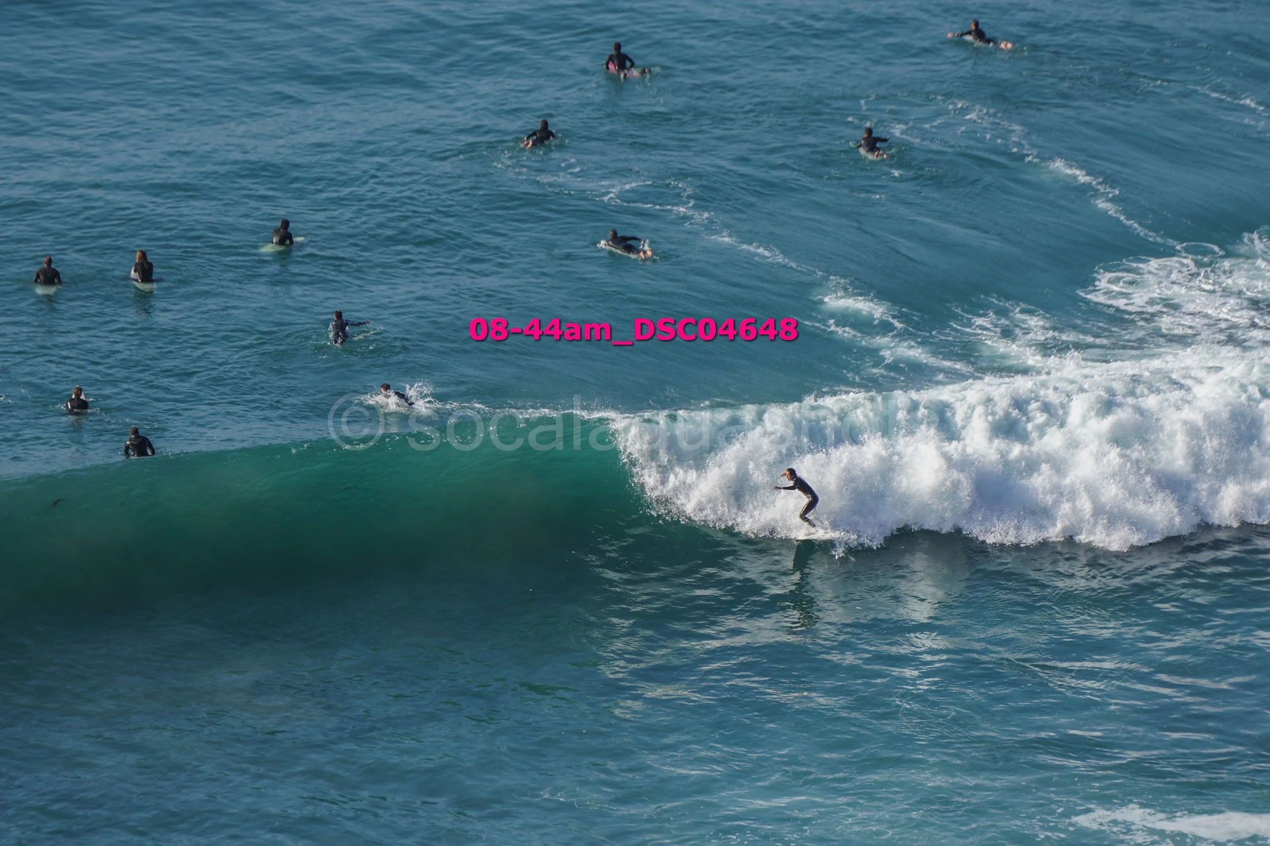 A surfer riding a wave with several people in the water watching in the background.
