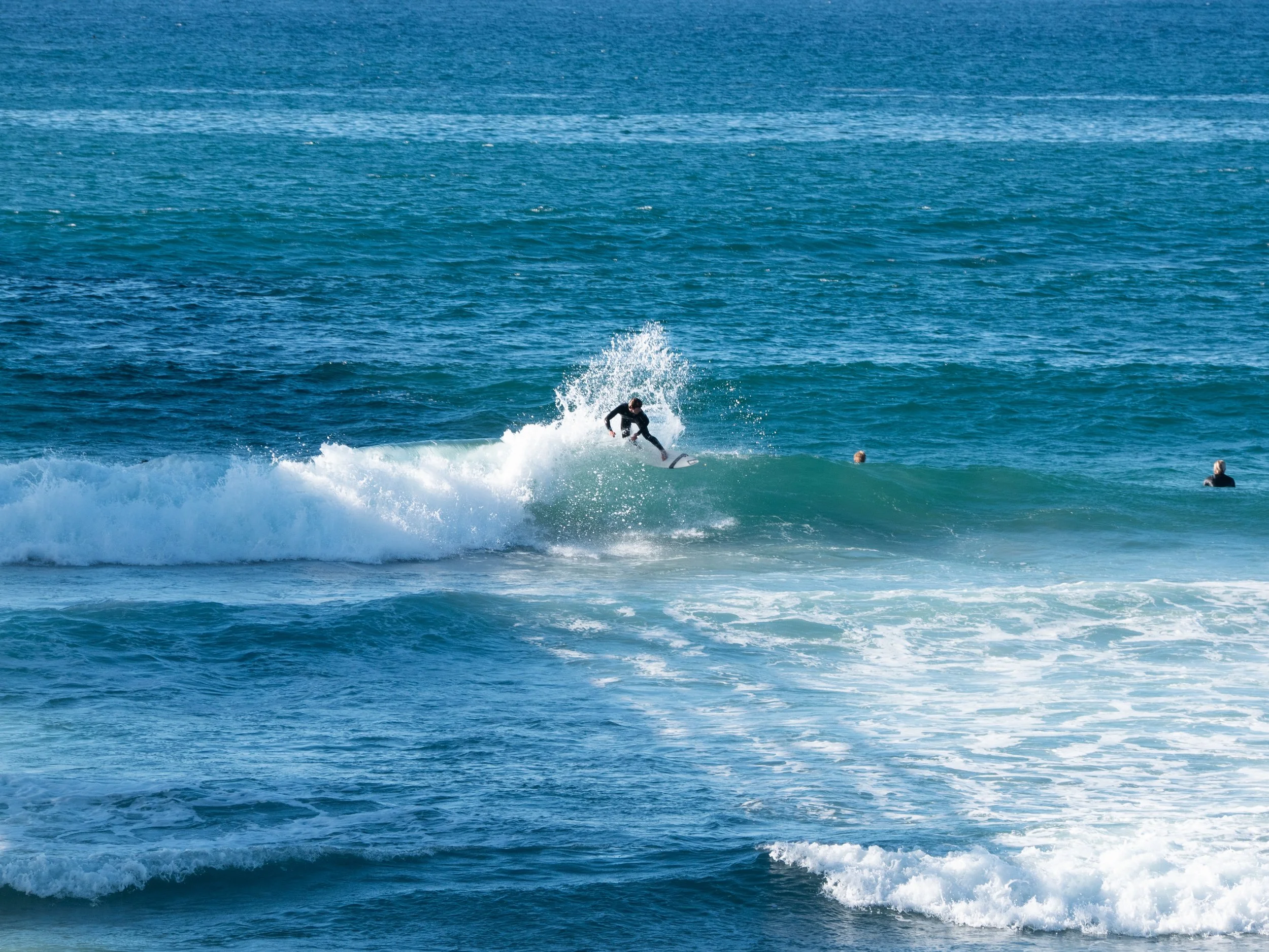 A person surfing on a wave in the ocean, with two other individuals in the water nearby.