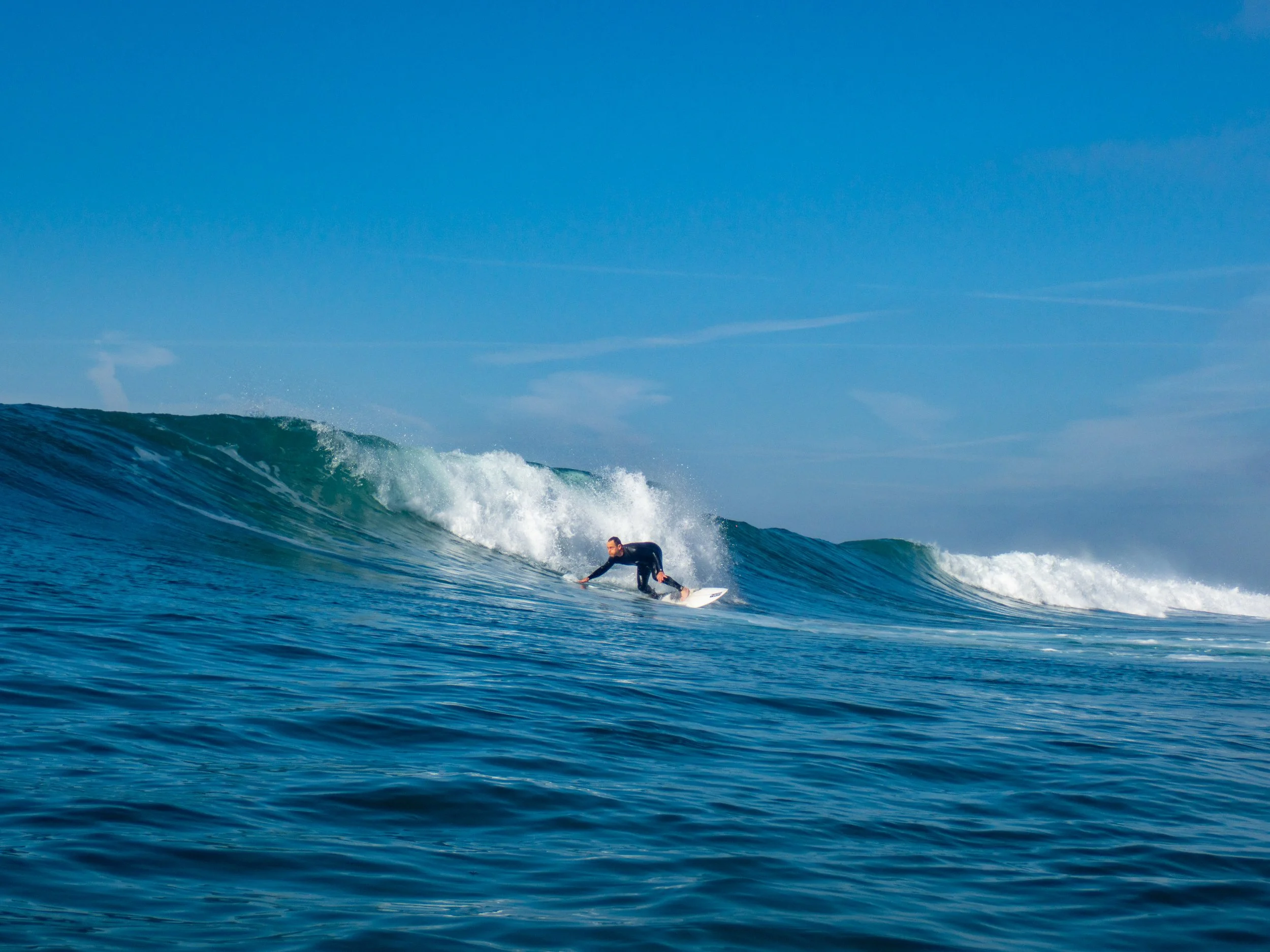 A person surfing on a wave in the ocean under a clear blue sky.