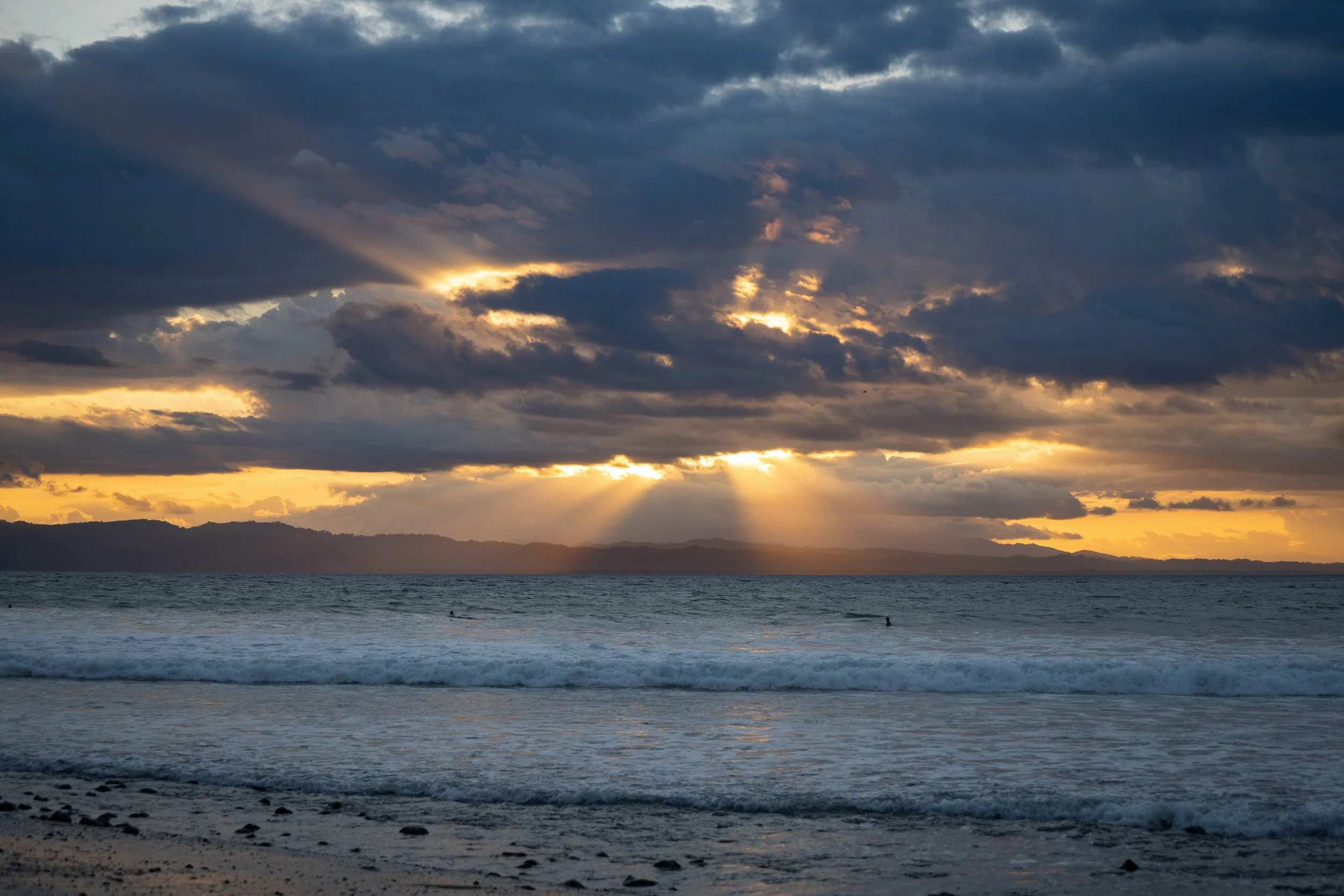 Sun rays breaking through dark clouds over the ocean at sunset.