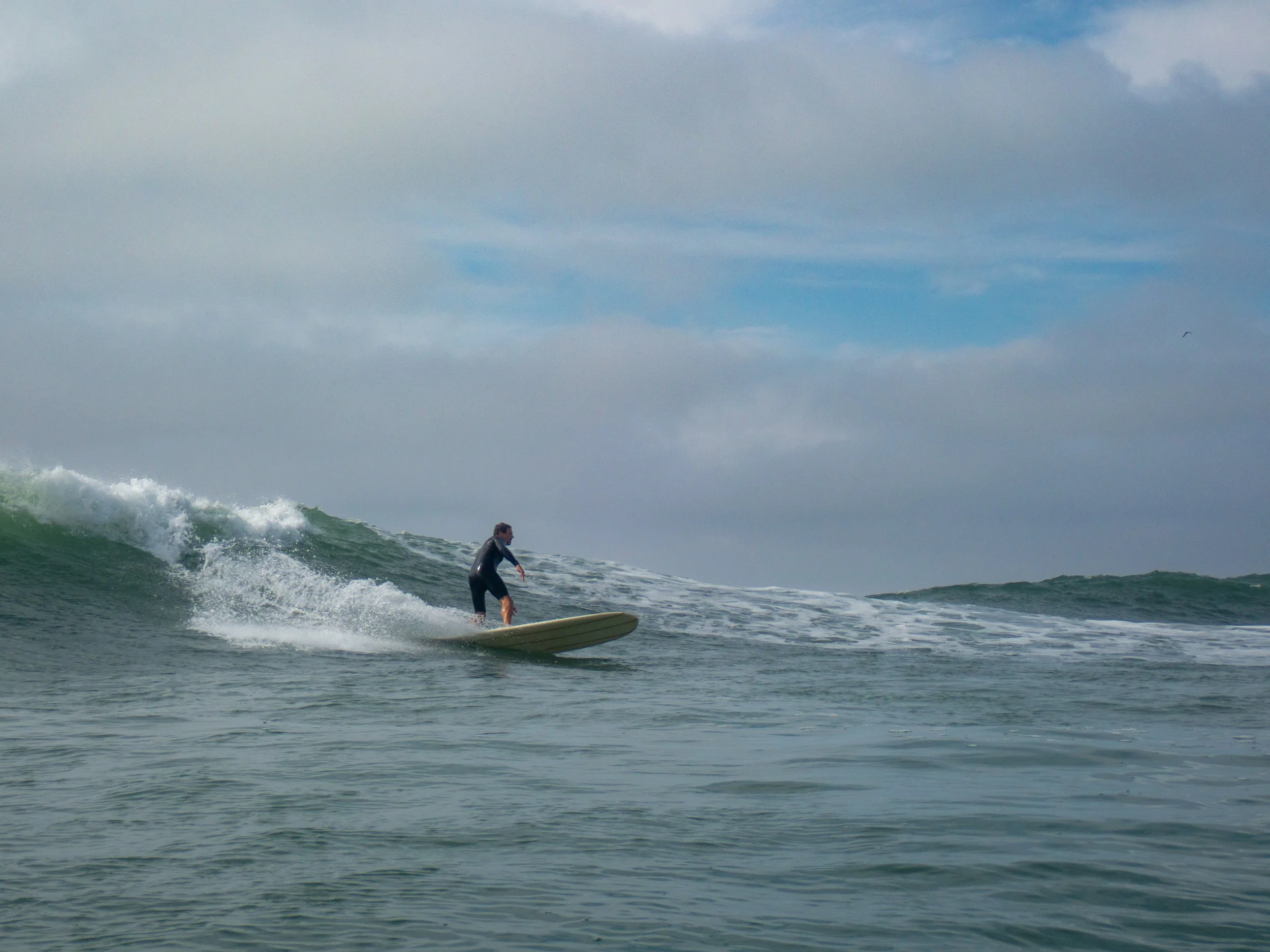 A person surfing on a wave in the ocean under a cloudy sky.