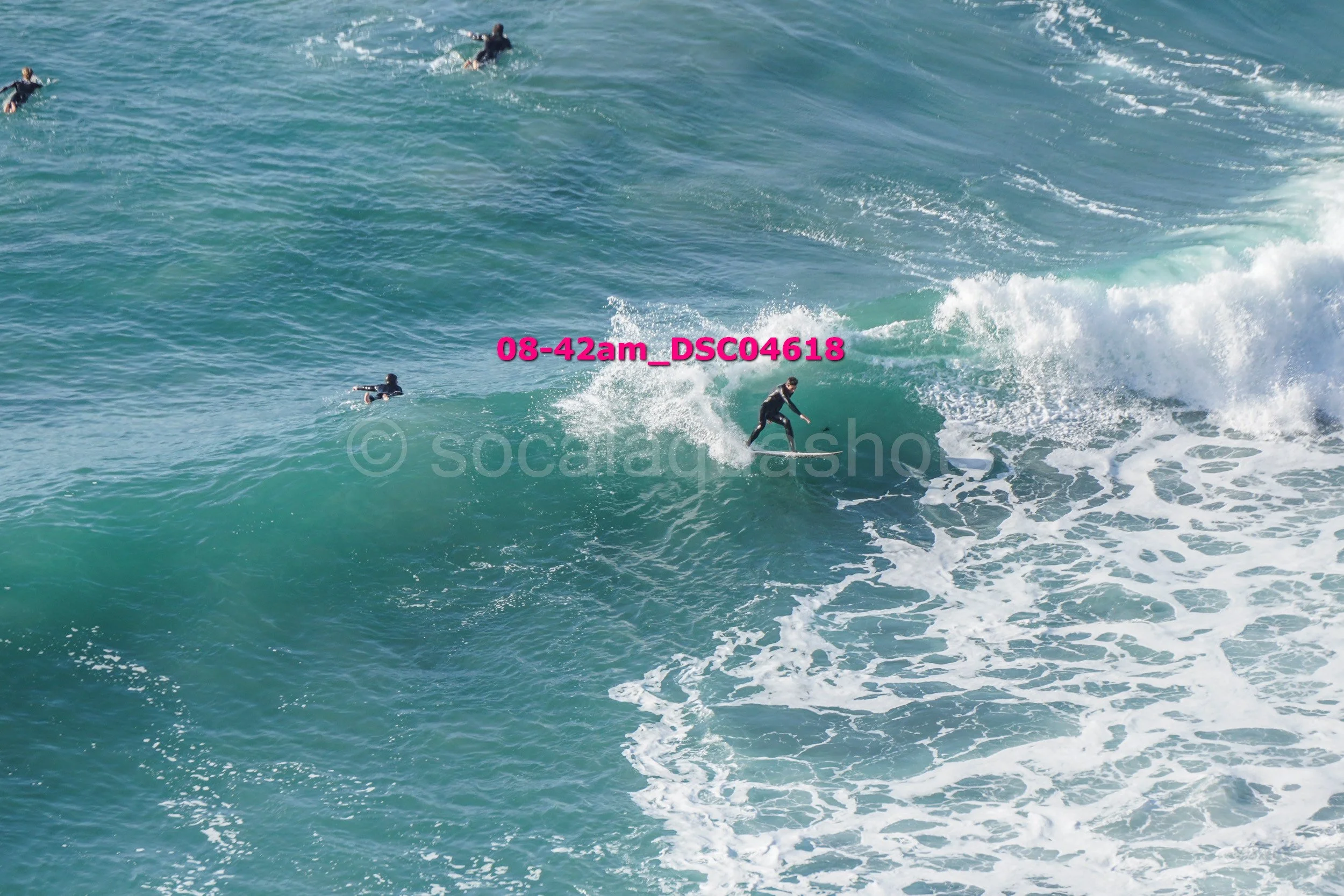 Surfer riding a wave with several other surfers in the water nearby.