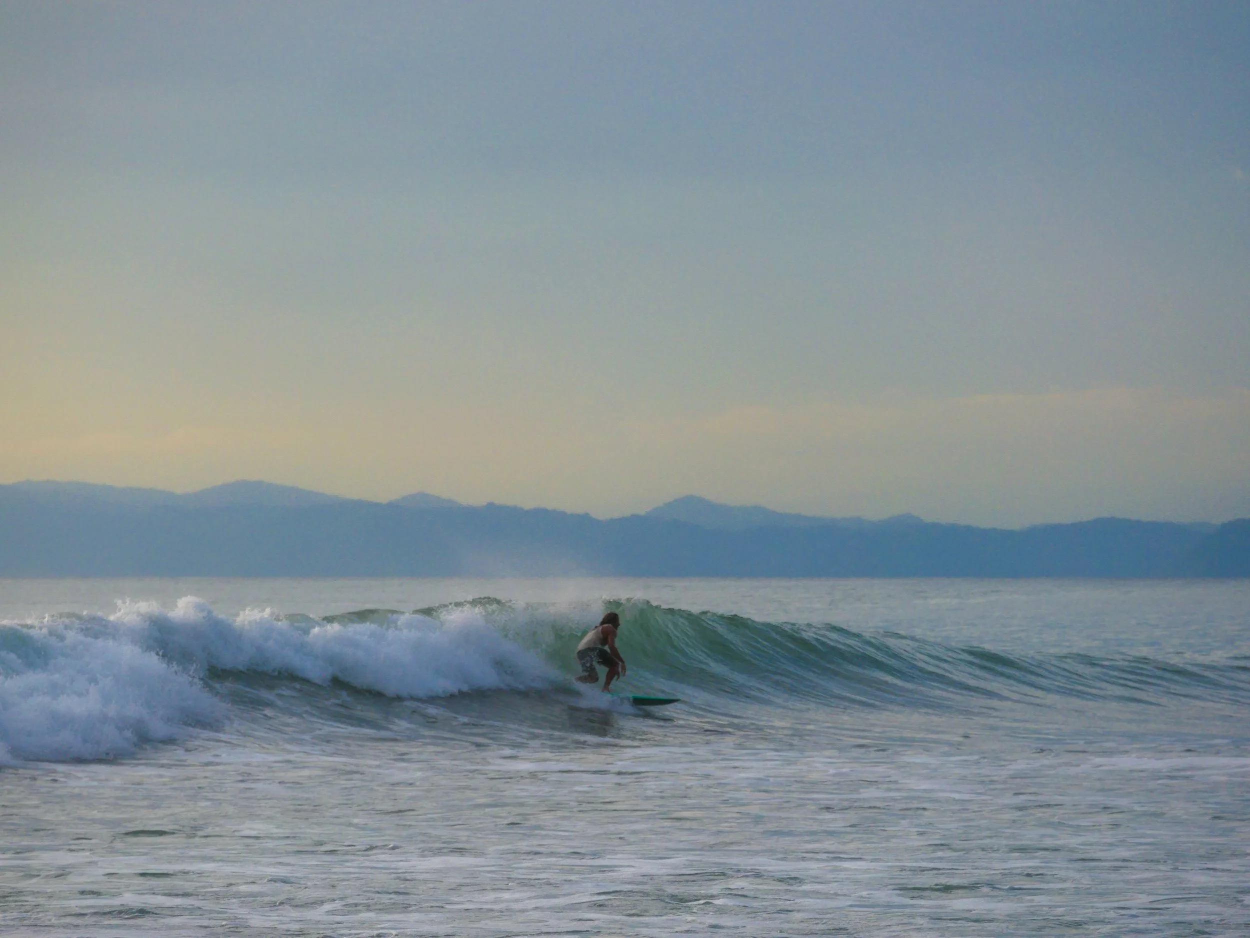 Surfer riding a wave in the ocean with mountains in the background.