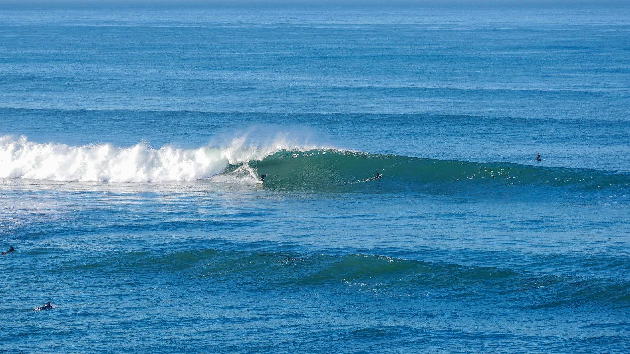 Surfer riding a wave in the ocean with others watching nearby
