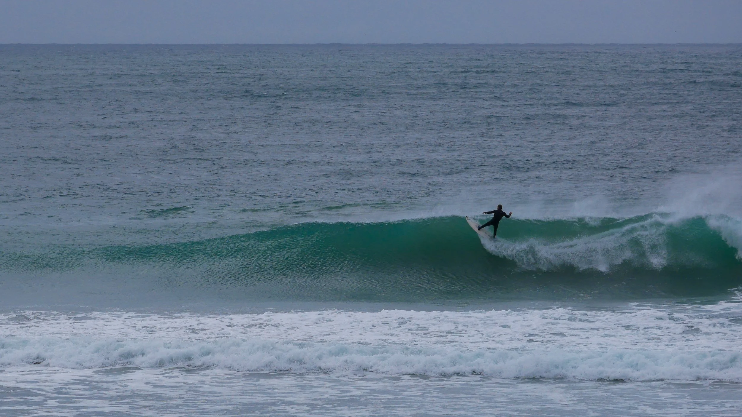 Person surfing on a wave in the ocean, overcast sky.