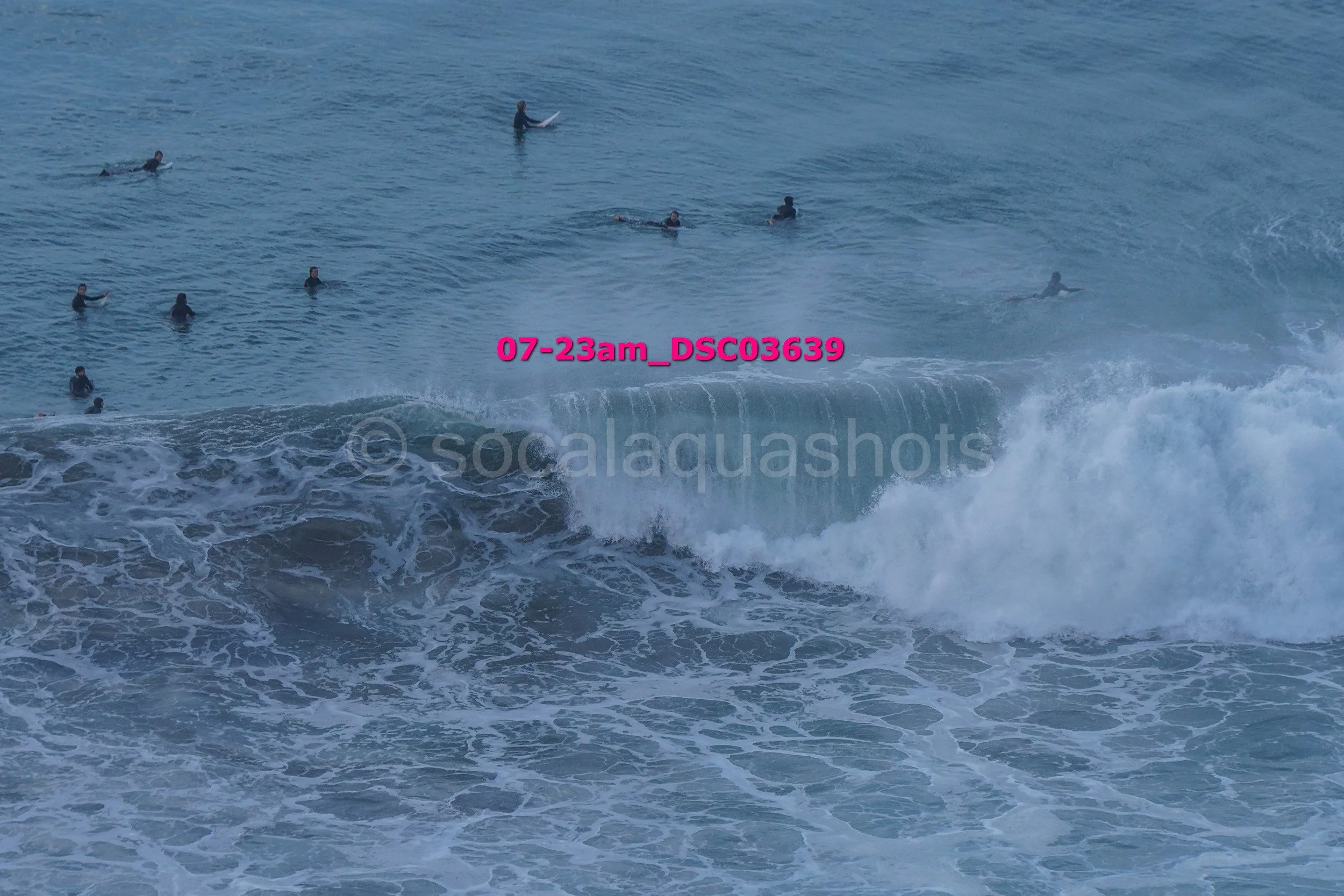 People surfing in the ocean on a cloudy day with waves breaking and surfboards visible.