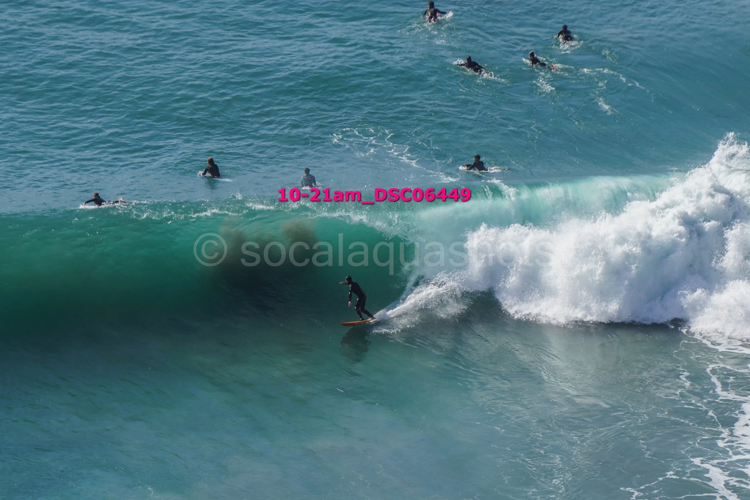 Surfer riding a large wave with several surfers in the background in the ocean.