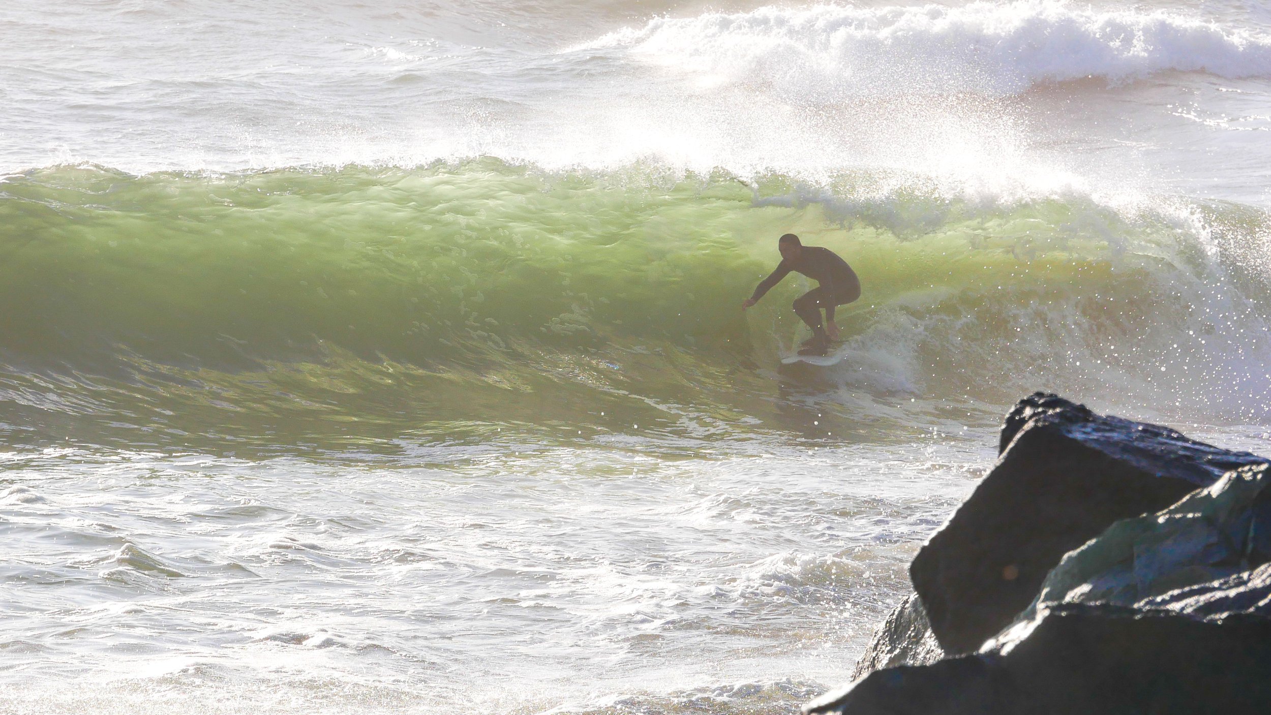 Surfer riding a wave near rocky shore