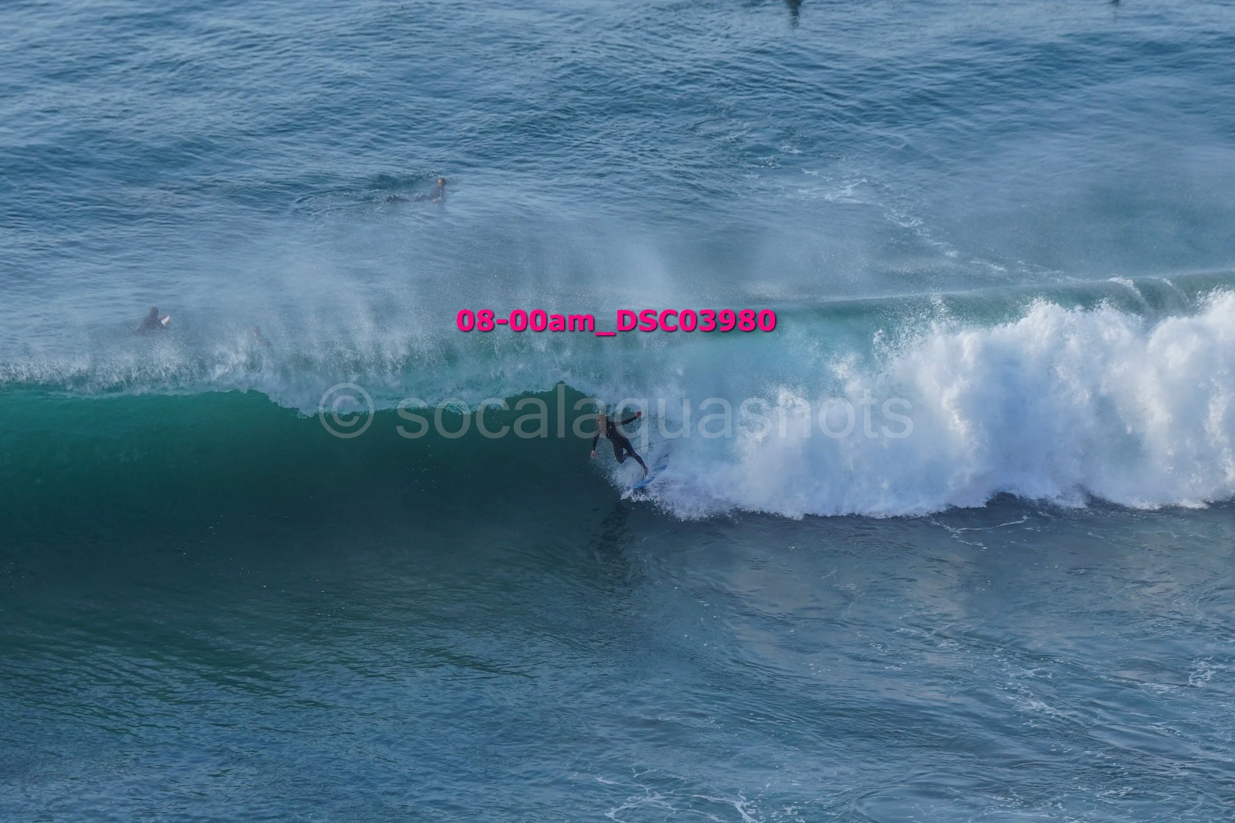 Surfer riding a wave in the ocean, with two other surfers visible in the water.