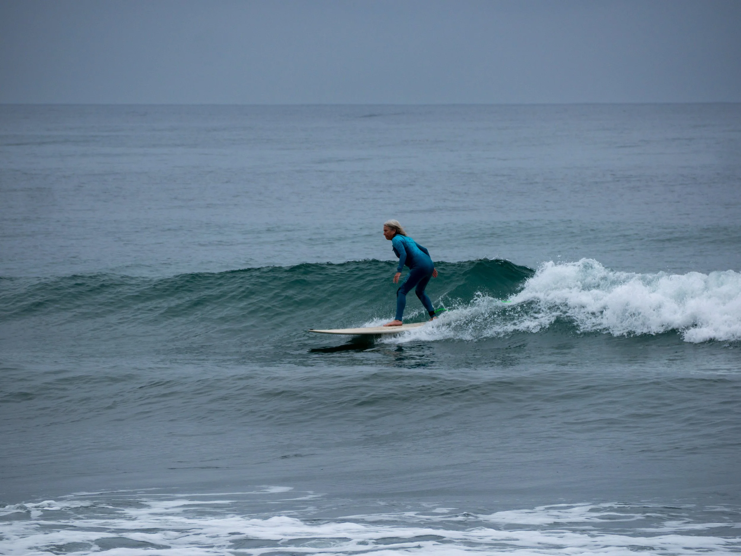 A woman surfing on a small wave in the ocean, wearing a blue wetsuit.