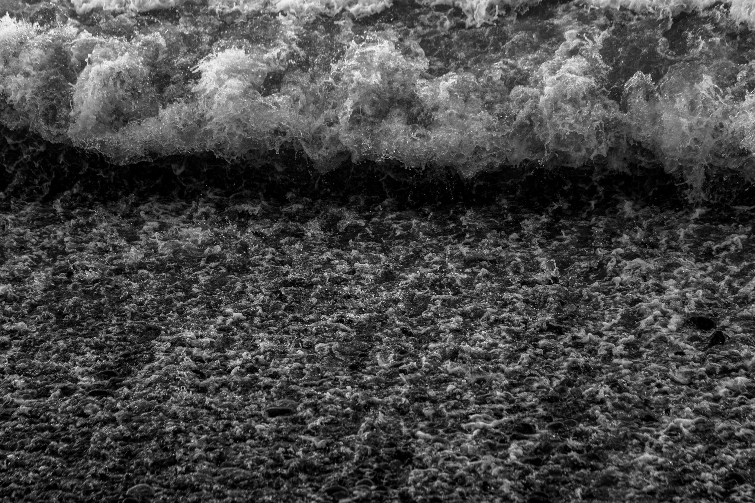 Black and white photo of ocean waves crashing onto a rocky shoreline.