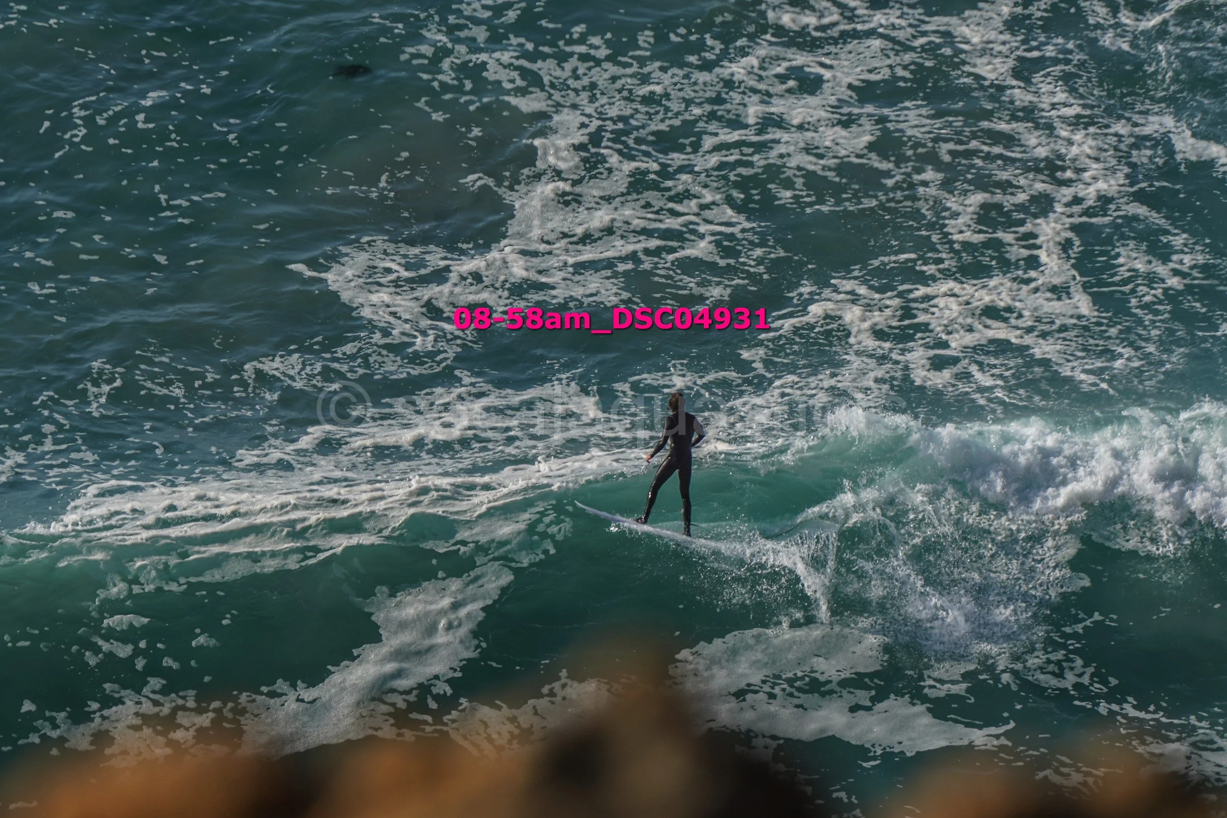 Person surfing on a wave in the ocean, seen from above.
