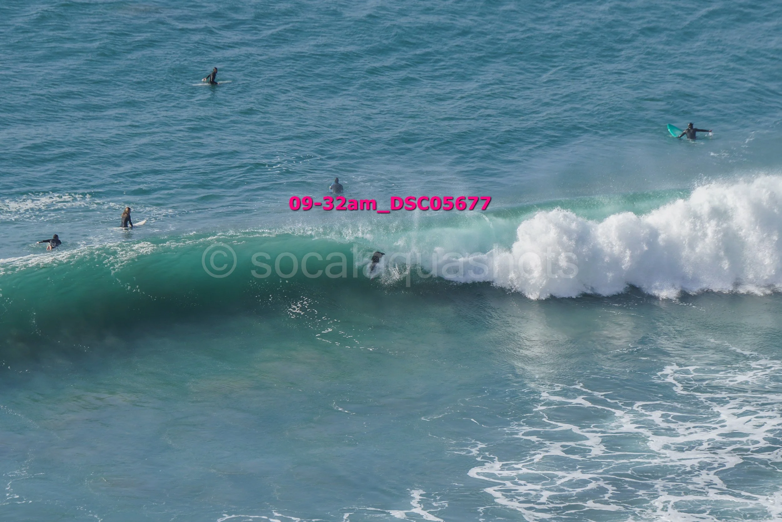 Group of people surfing and swimming in the ocean, with one person riding a wave.