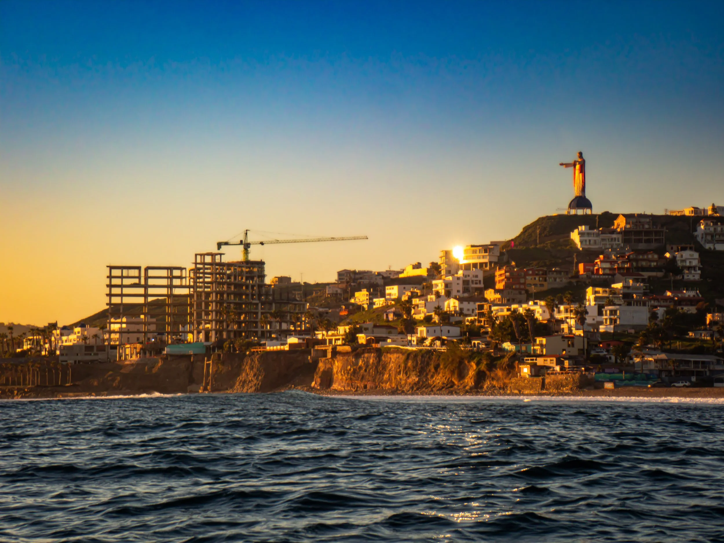 San Diego bay at sunset with the Cristo Rey statue on a hill, construction site, buildings, and water in the foreground.