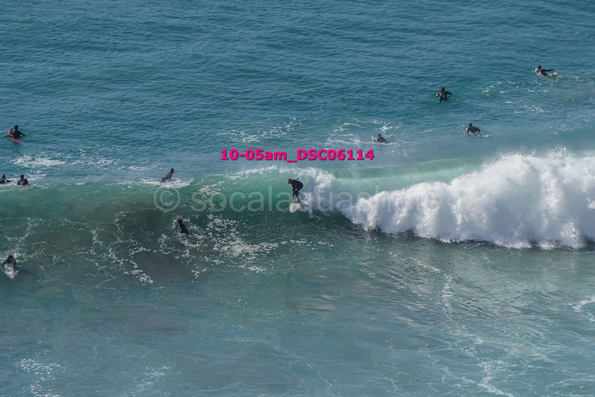 A surfer riding a wave while multiple surfers are in the water around him at the beach.