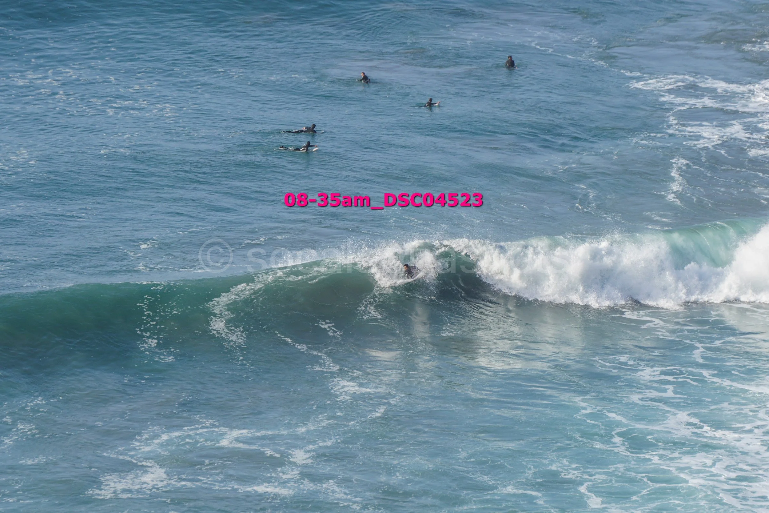 Surfer riding a wave with a group of people swimming in the ocean in the background.