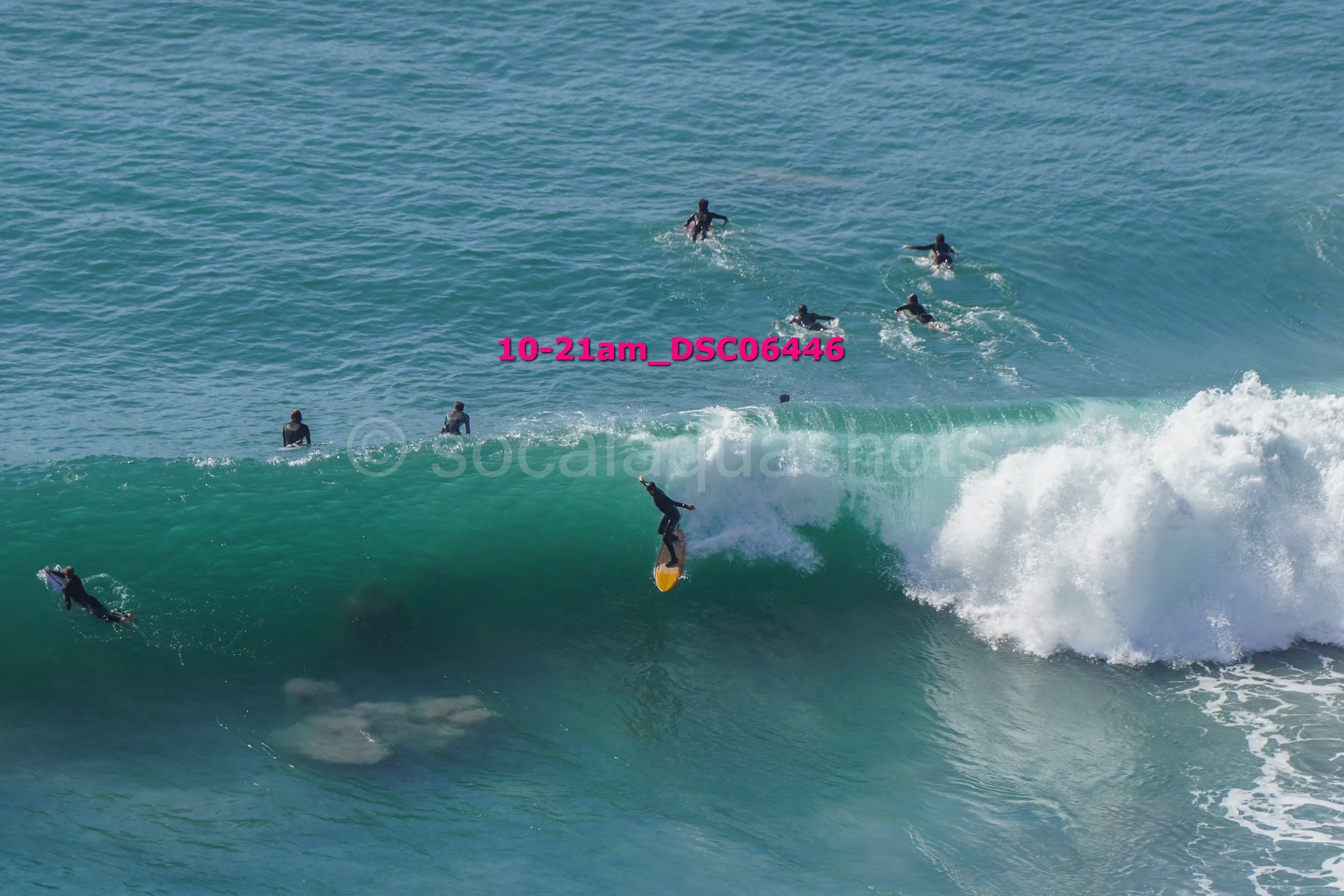 A group of surfers in wetsuits riding and paddling on large ocean waves during daytime.