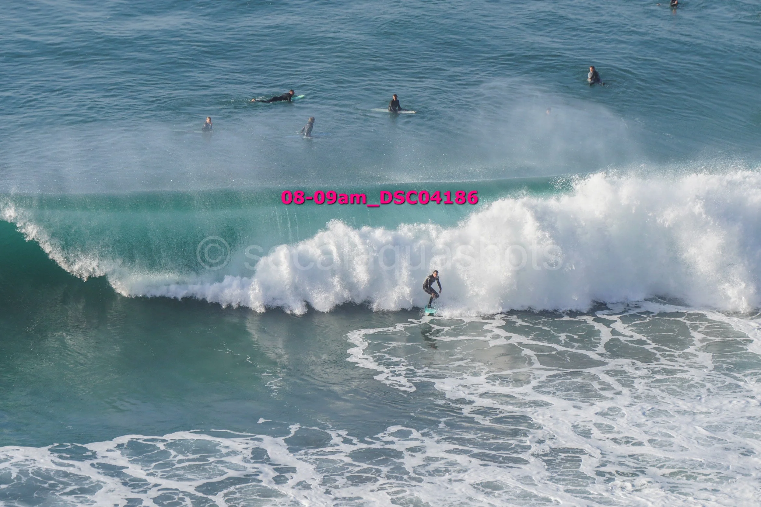 A person surfing on a large wave with several other surfers in the water in the background.