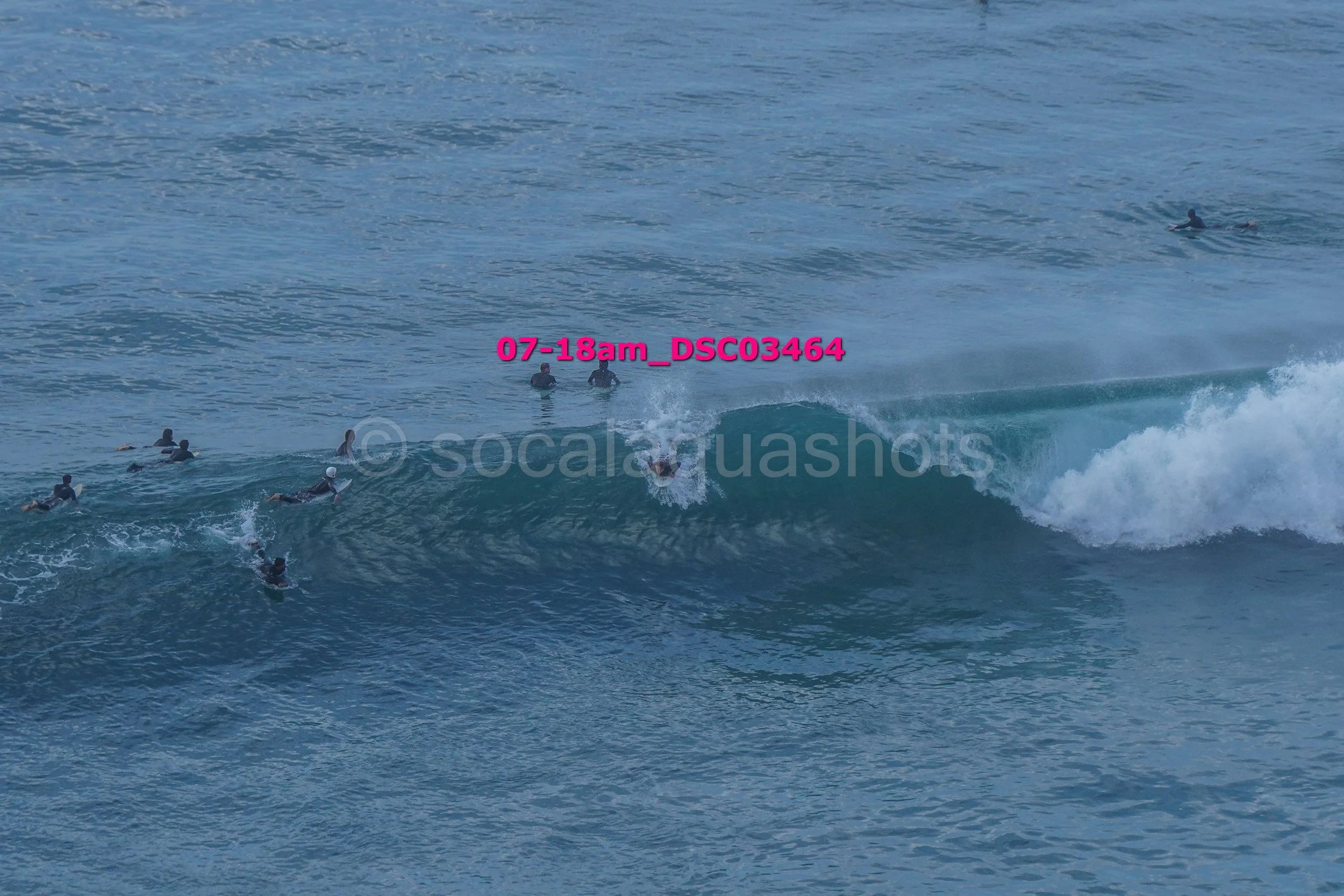 Multiple surfers in the ocean, some waiting for waves and one surfing a wave.