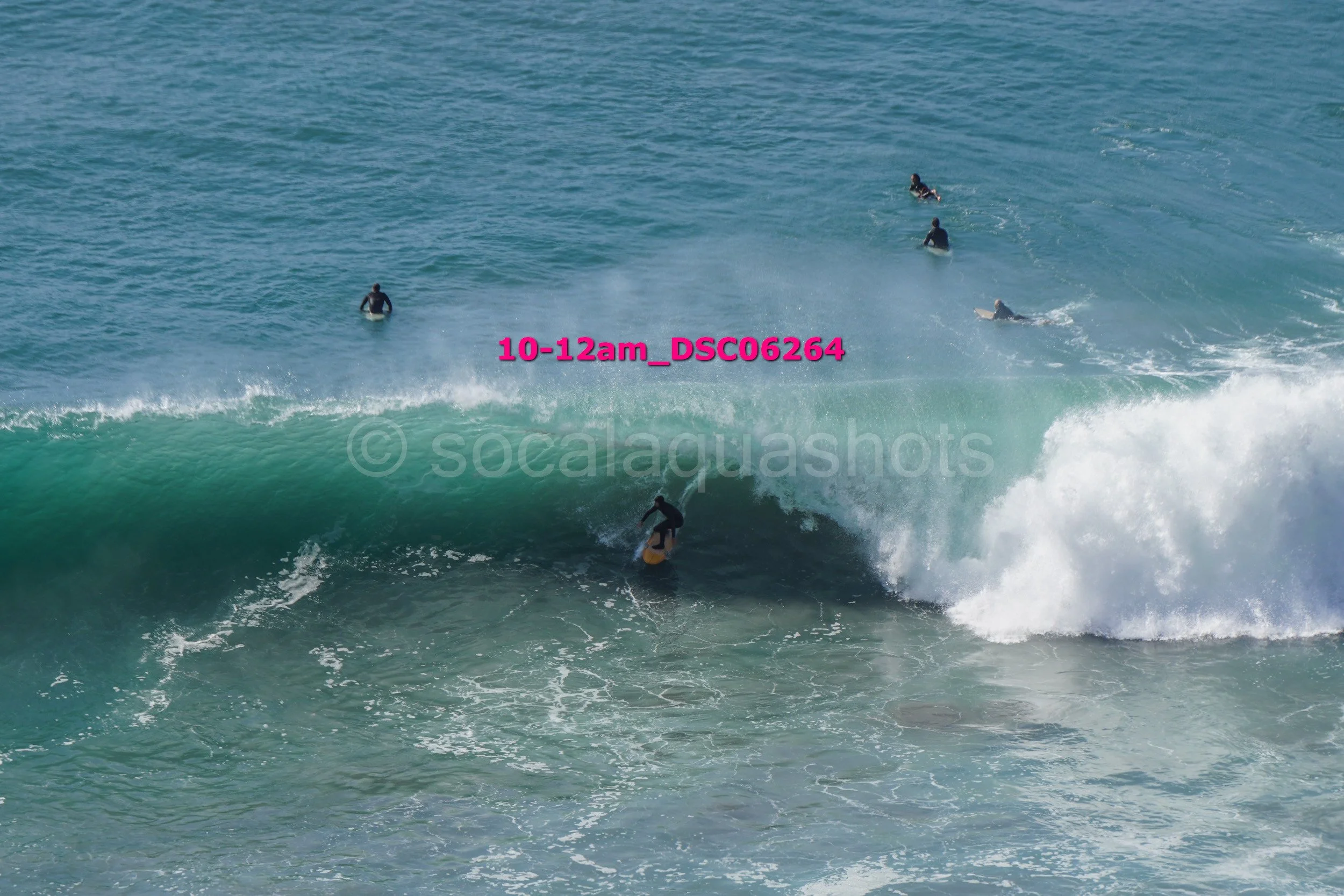Surfer riding a large wave with several other surfers in the water nearby on the ocean.