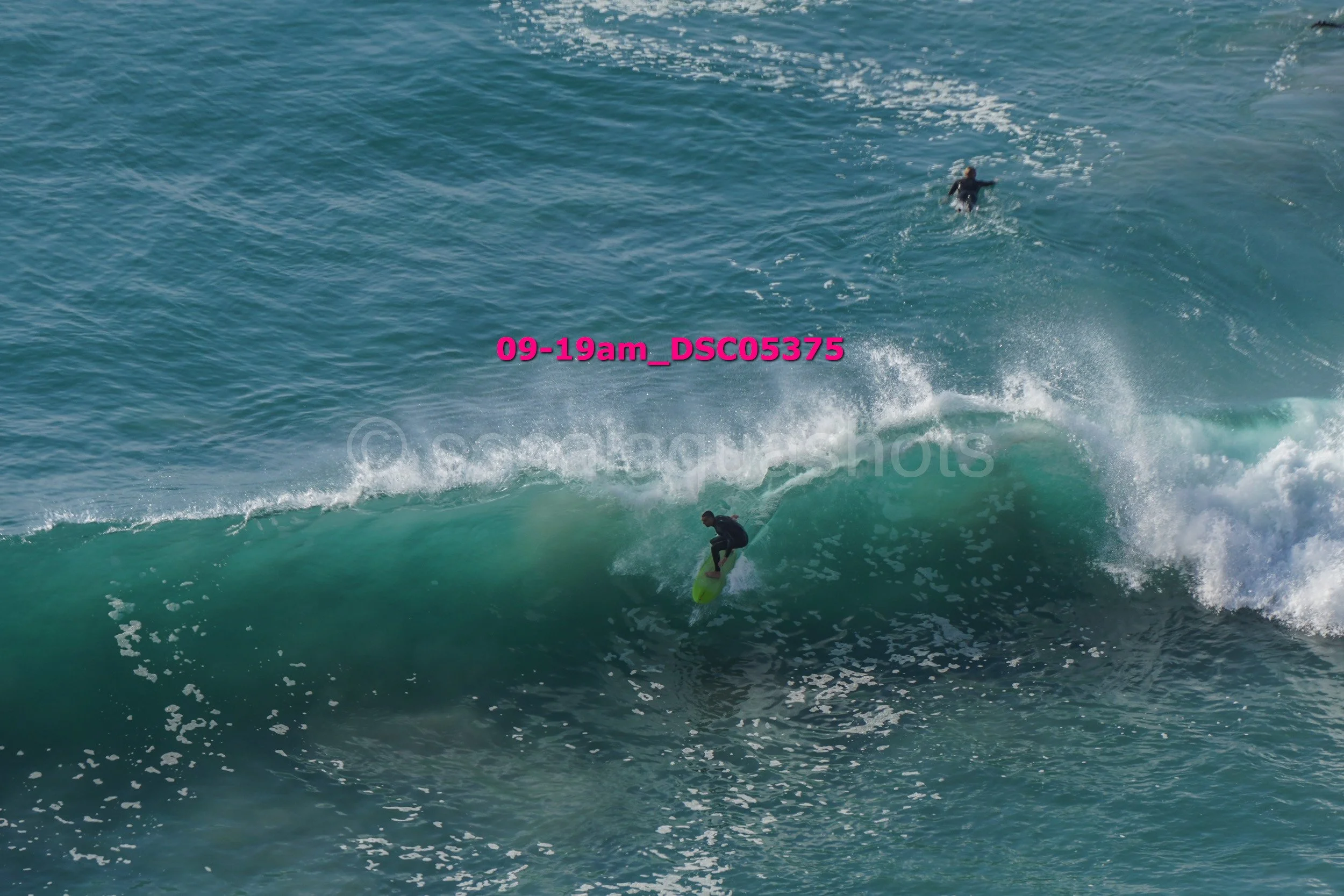 A person surfing on a wave in the ocean with another person swimming in the background.