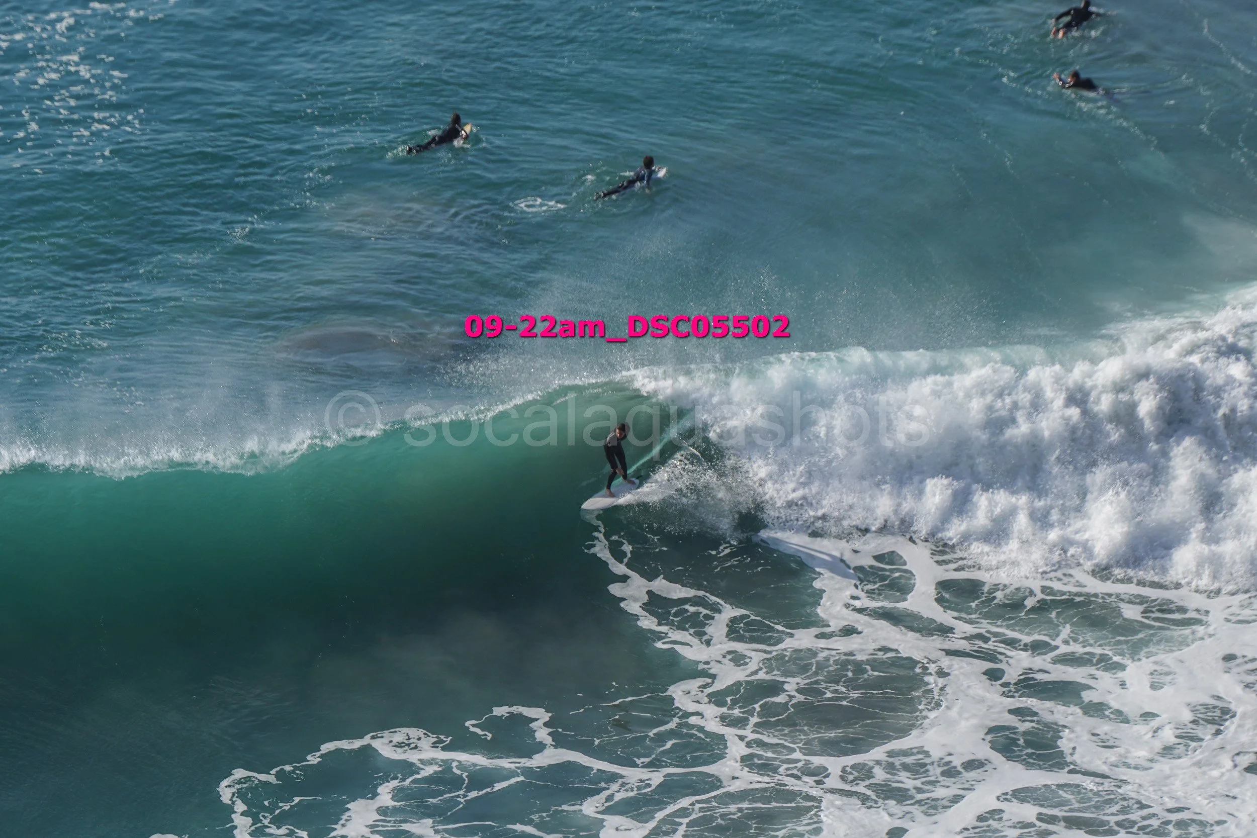 A surfer riding a wave with several surfers floating in the water in the background.