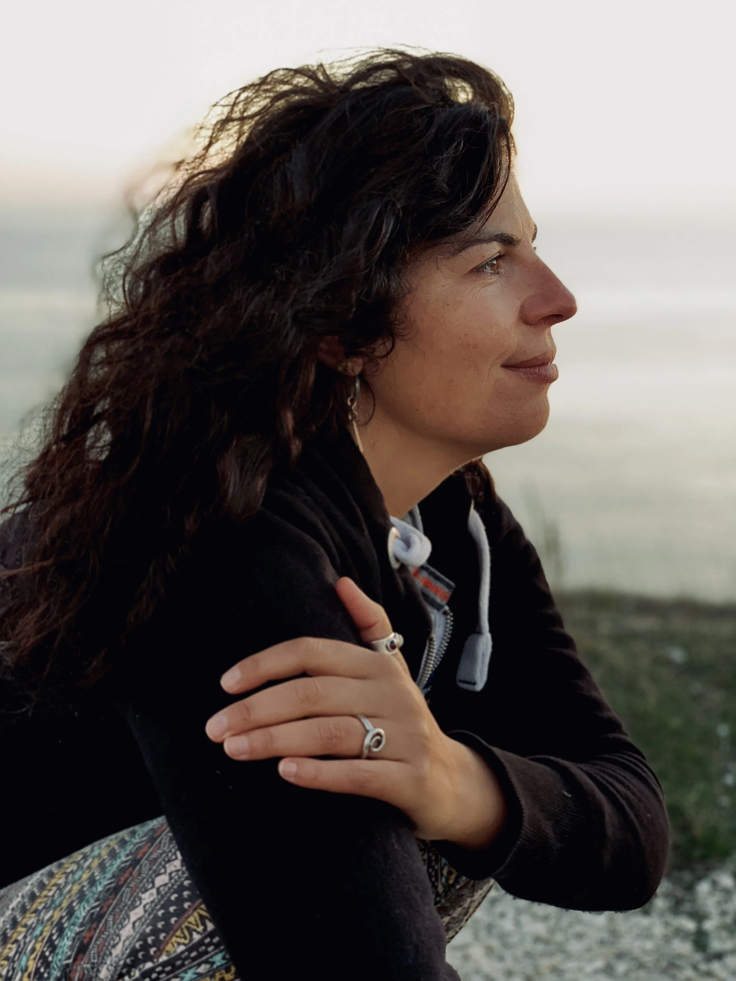 A white woman with black curly hair crouched down & looking into the distance