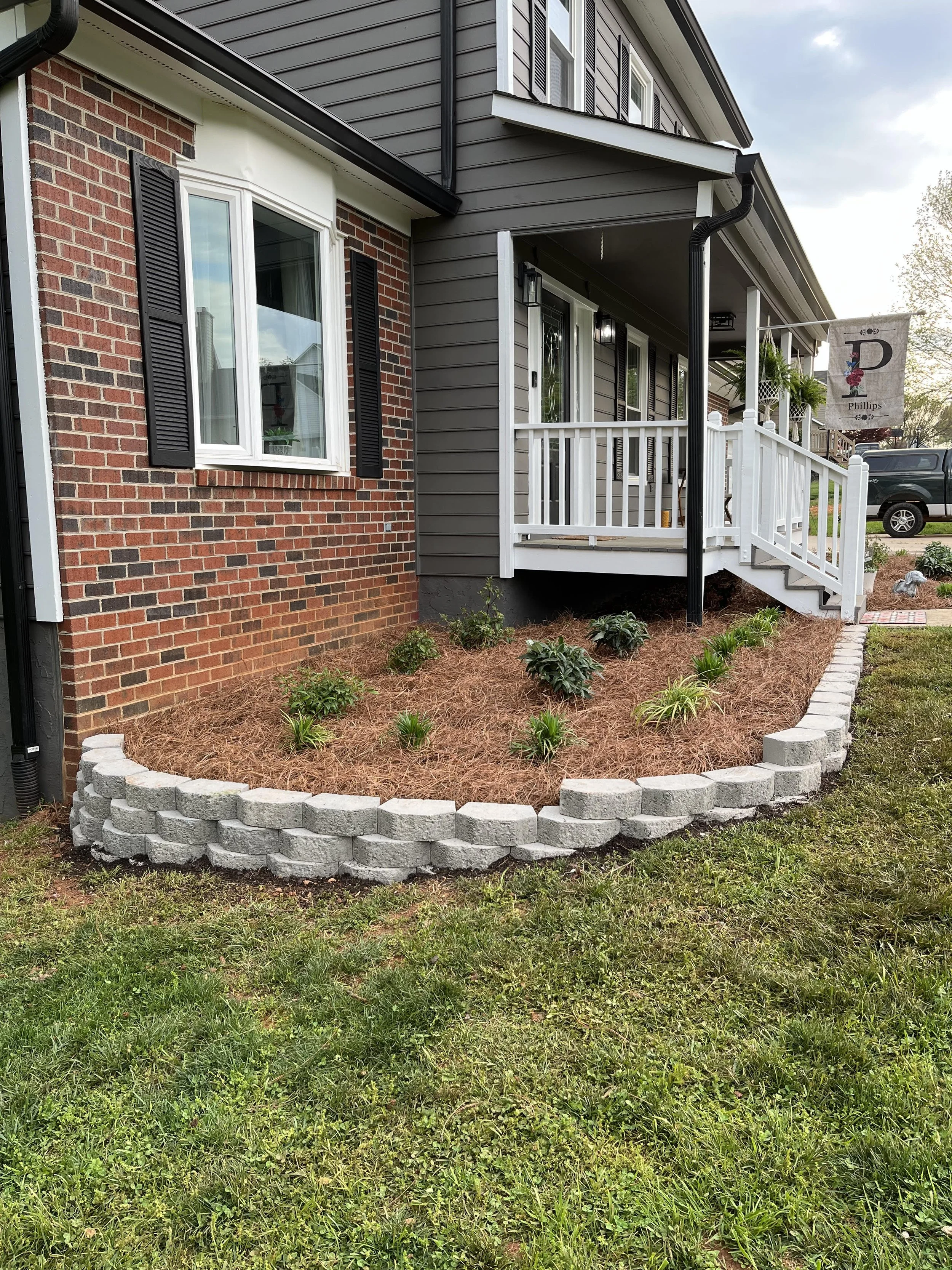 Landscaping services Hickory NC – small retaining wall garden bed with mulch, pine straw, and plant installation for residential yard