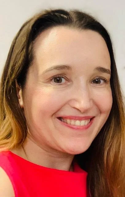 A smiling woman with long brown hair in a red top, close-up portrait.
