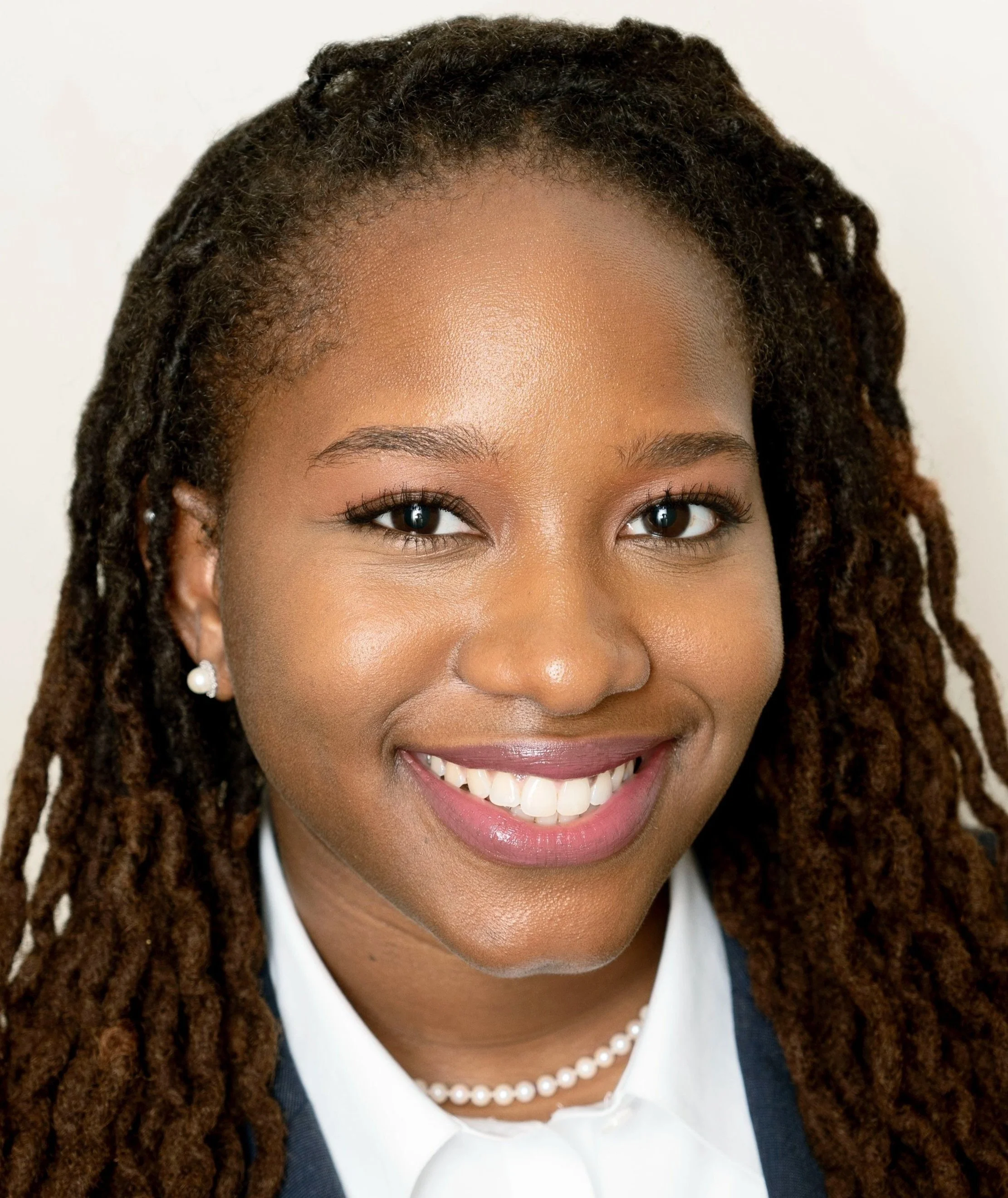 A photo of attorney Ptahra Jeppe, a woman with rich brown skin, wavy locs, pearls, and a bright smile