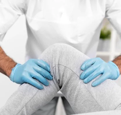 Medical professional examining a person's knee with gloved hands in a clinical setting