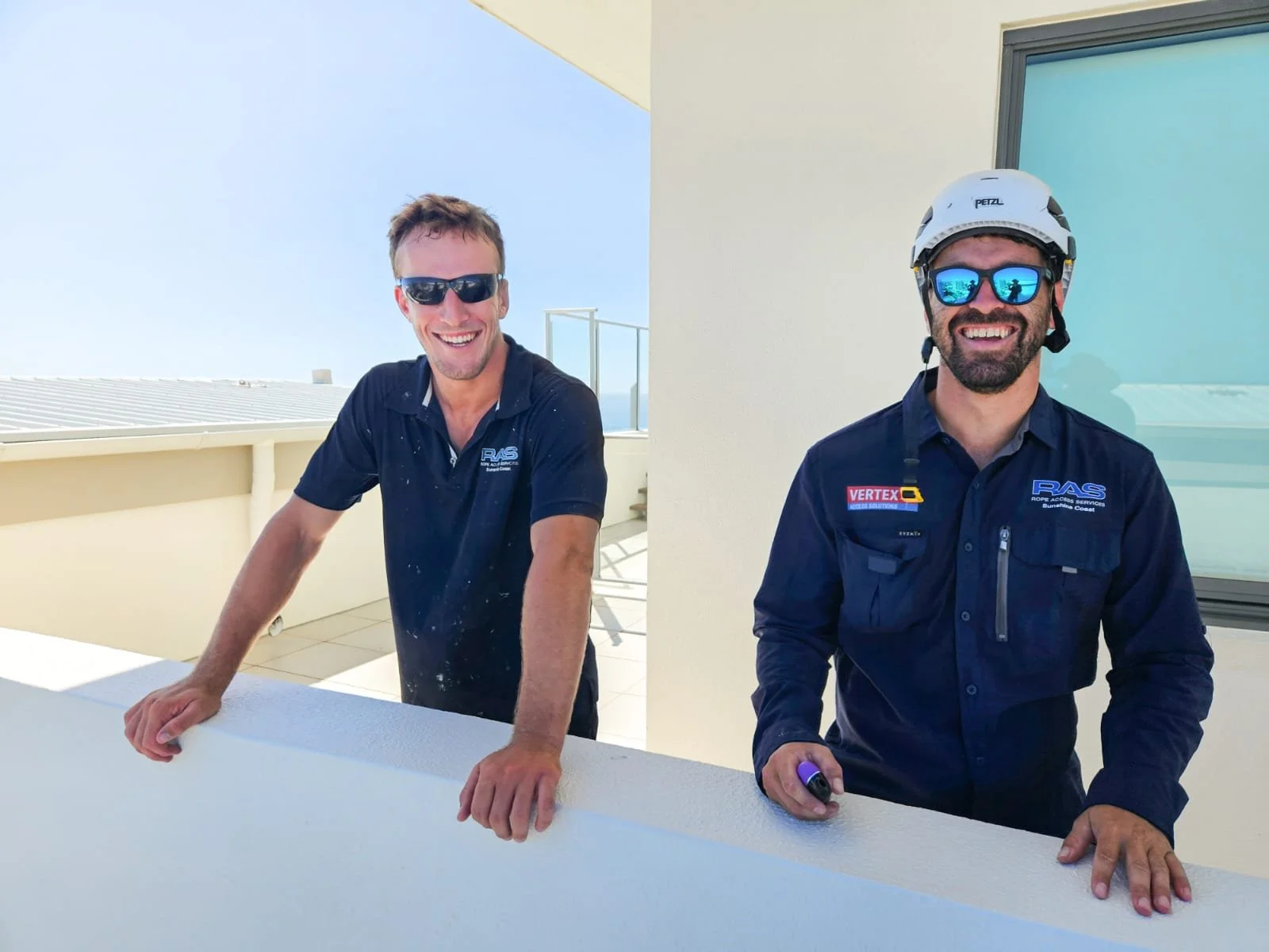Two rope access technicians smiling after completing a window clean on a Sunshine Coast commercial project, delivering spotless results and ensuring client satisfaction.