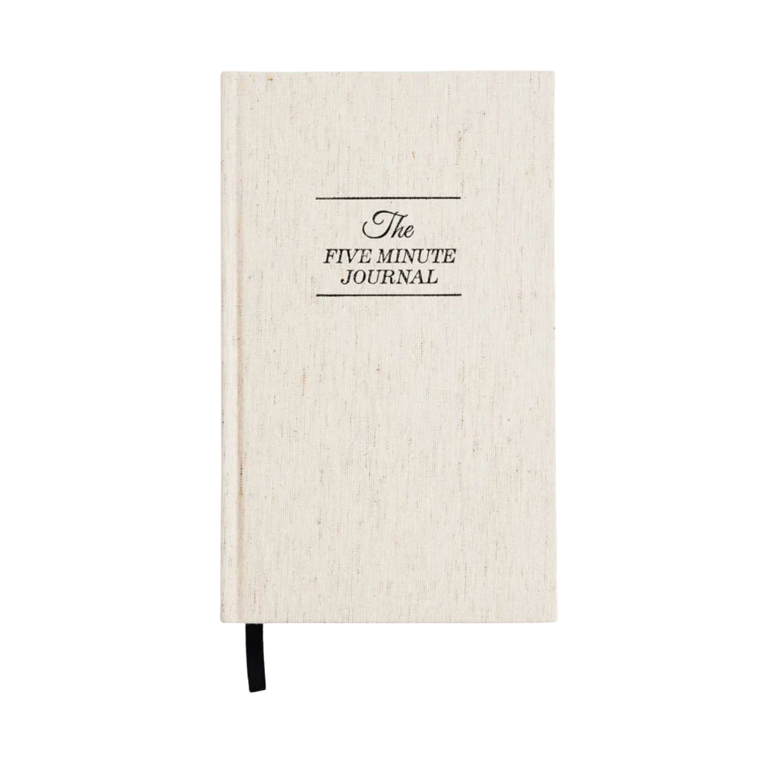 A cream linen hardcover journal with "The Five Minute Journal" embossed in black serif typography.