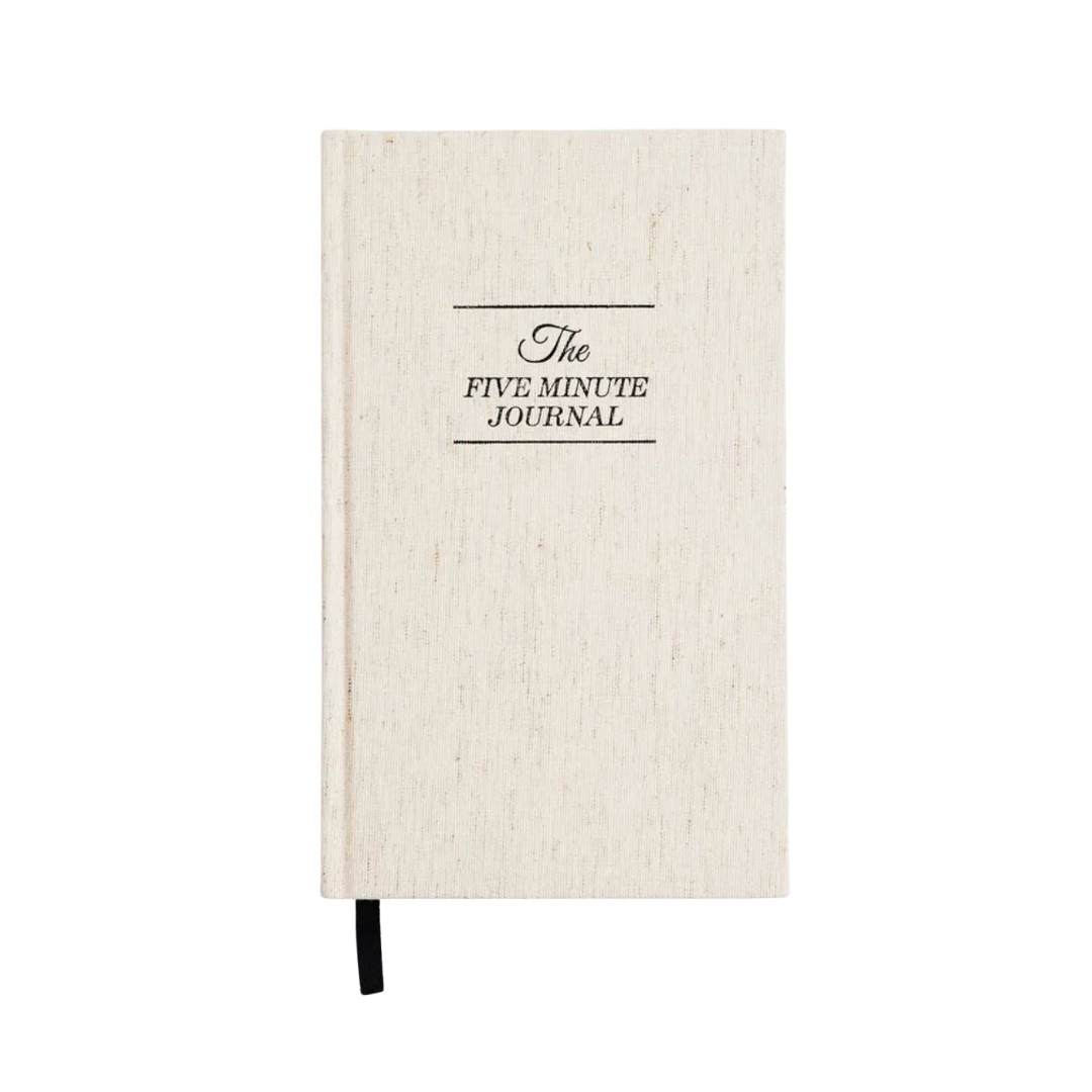 A cream linen-bound journal with "The Five Minute Journal" printed in black serif text on the cover.