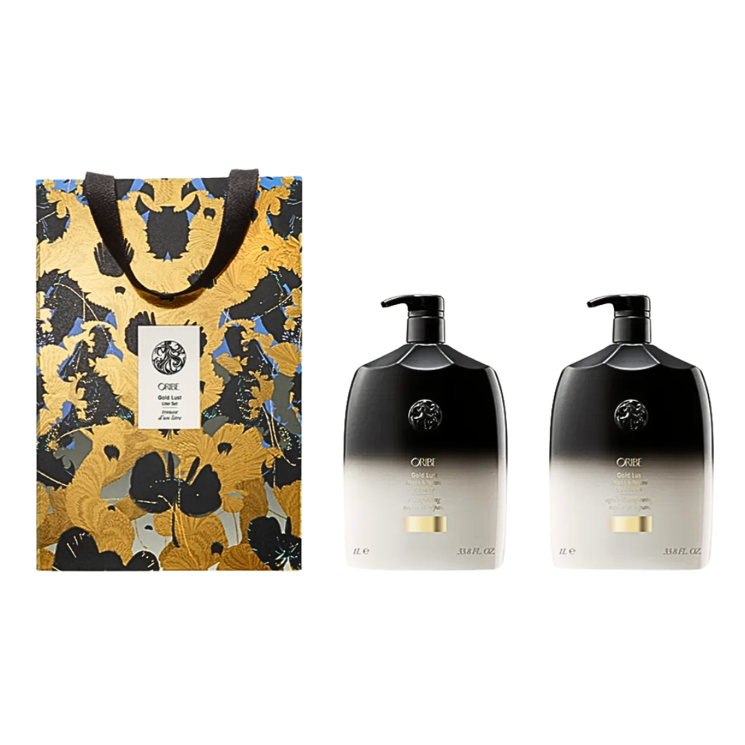 An Oribe gift set featuring a gold and black patterned shopping bag next to two signature black-to-clear gradient shampoo and conditioner bottles.